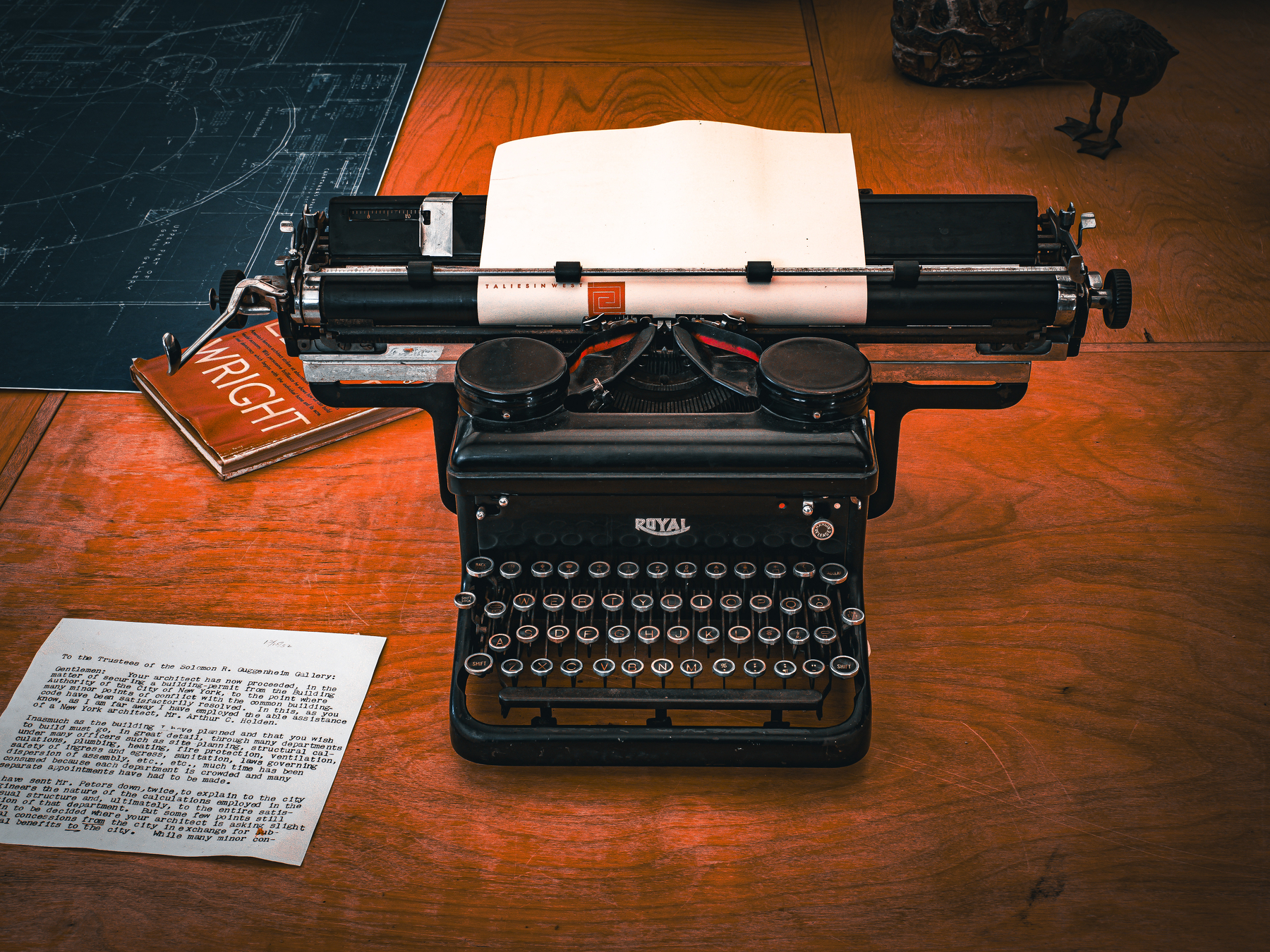 Auto-generated description: A vintage typewriter sits on a wooden table alongside typed and handwritten papers.