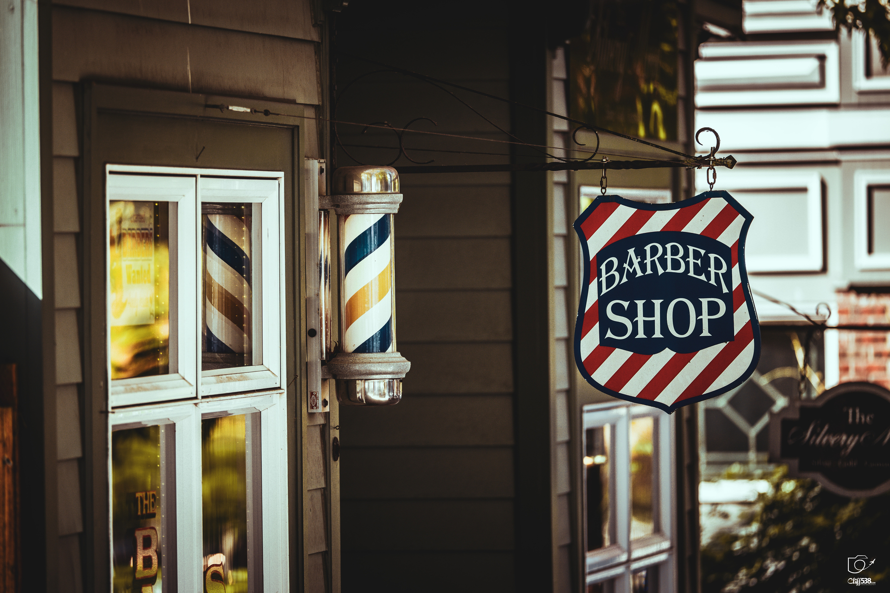 Auto-generated description: A vintage-style barber shop sign and barber pole are mounted outside a building.