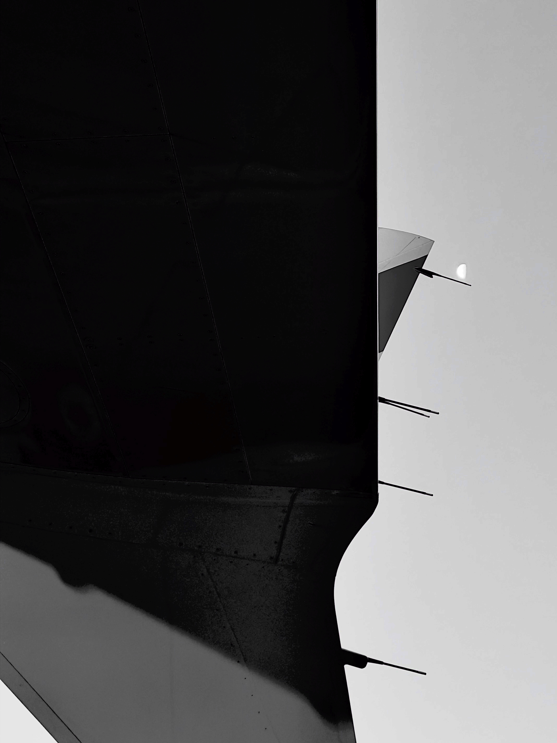 Auto-generated description: A silhouetted aircraft tail fin is juxtaposed against a bright sky with a small moon visible in the background.