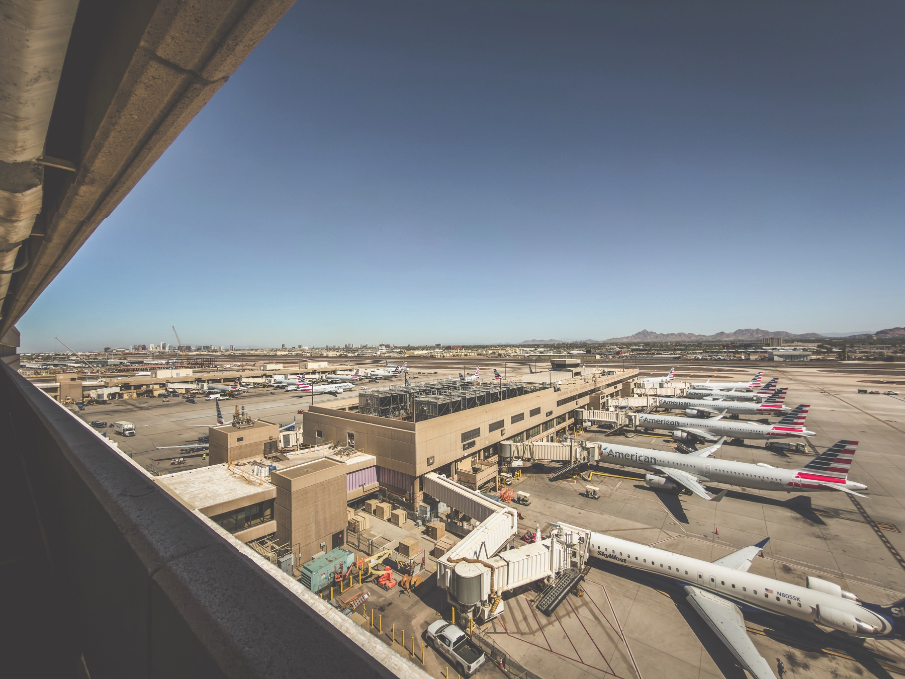 Auto-generated description: Several airplanes are parked at an airport terminal under a clear blue sky.
