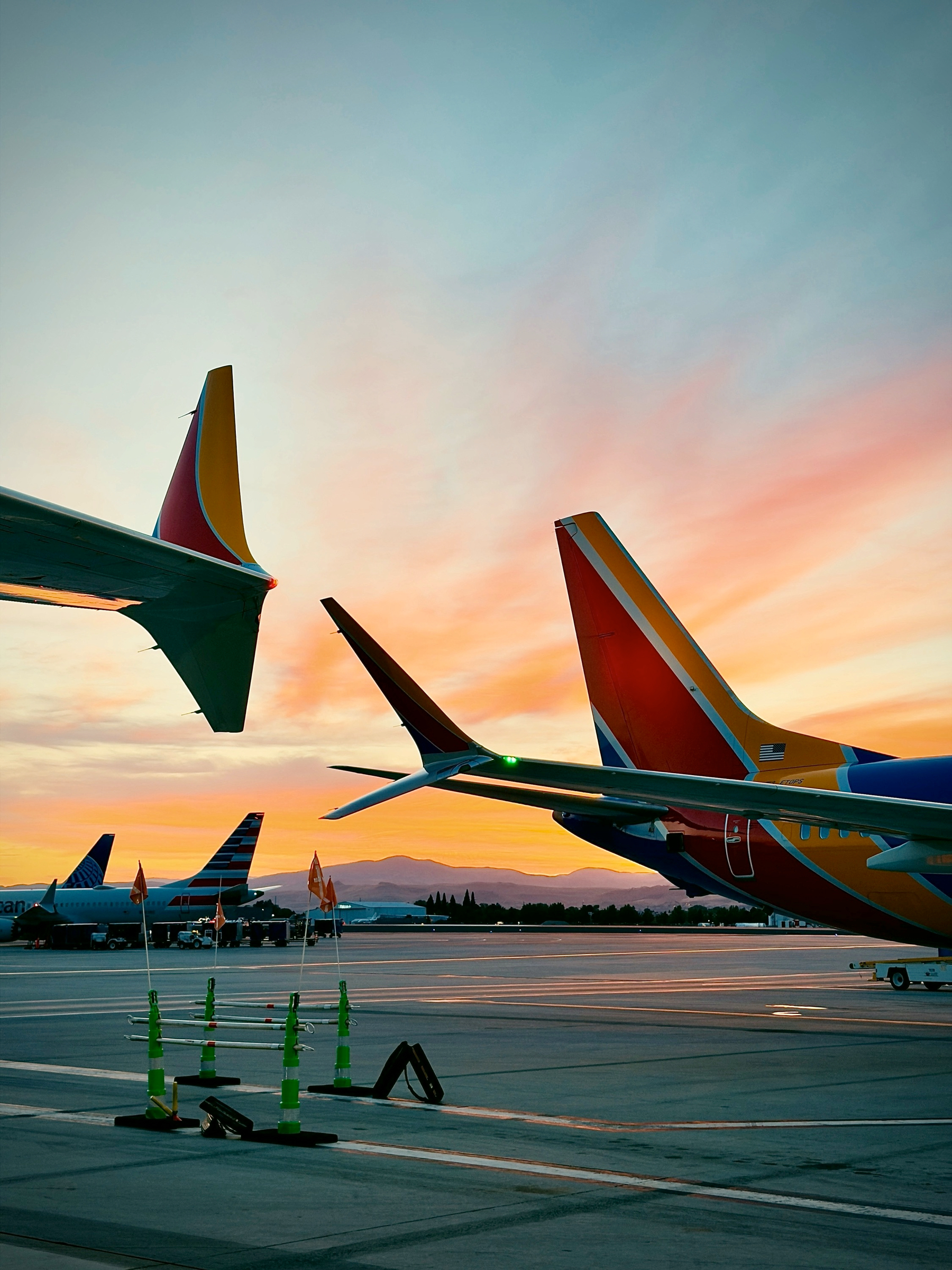 Auto-generated description: Several airplanes are parked on the tarmac during a colorful sunset with mountains in the background.