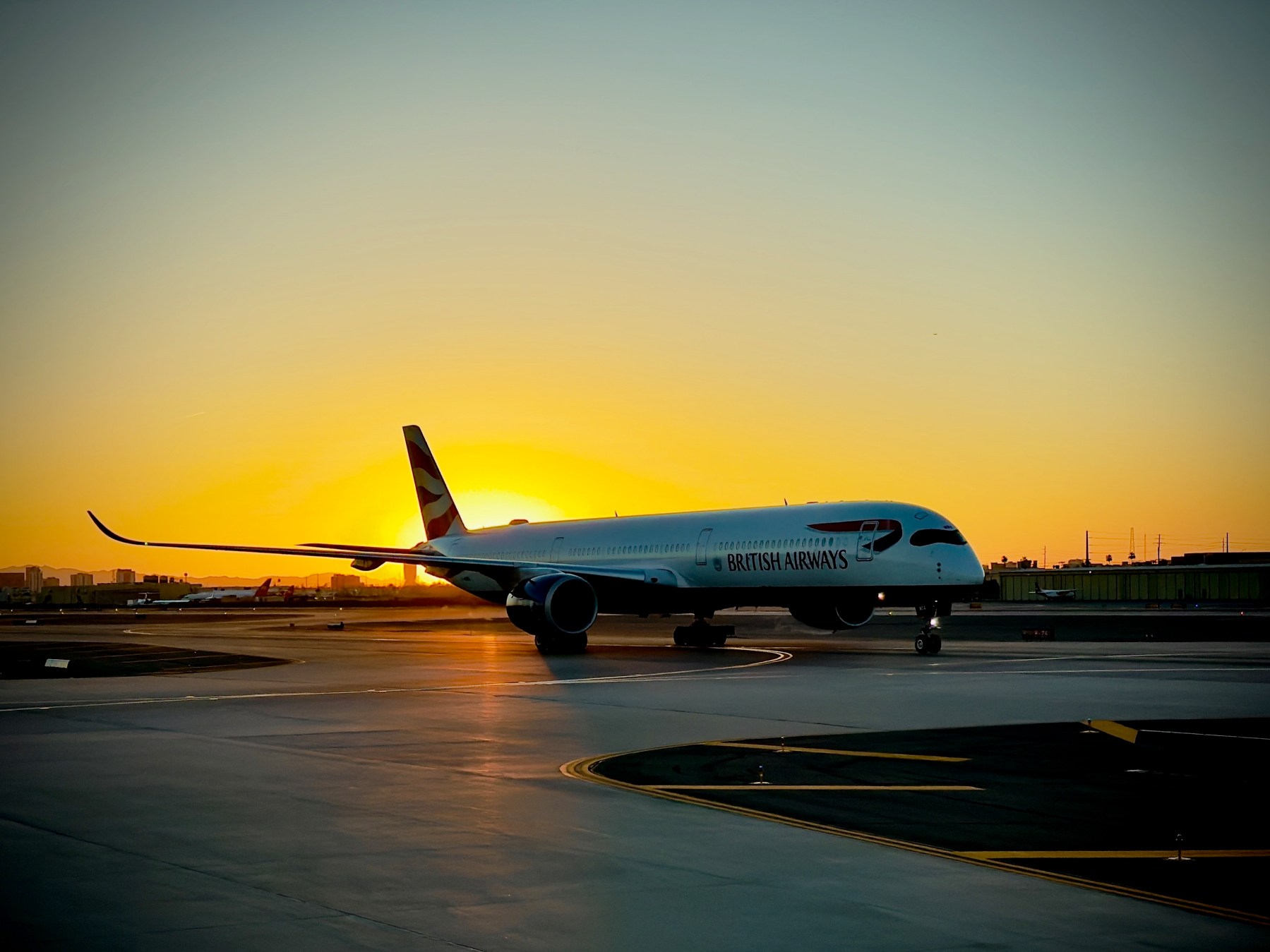 Auto-generated description: A British Airways airplane is taxiing on the runway at sunset.