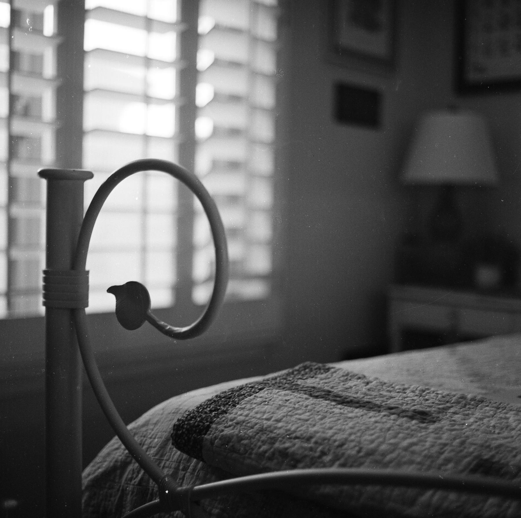 Auto-generated description: A vintage metal bed frame with a bird-shaped detail stands next to a bed covered with a quilt in a softly lit bedroom.