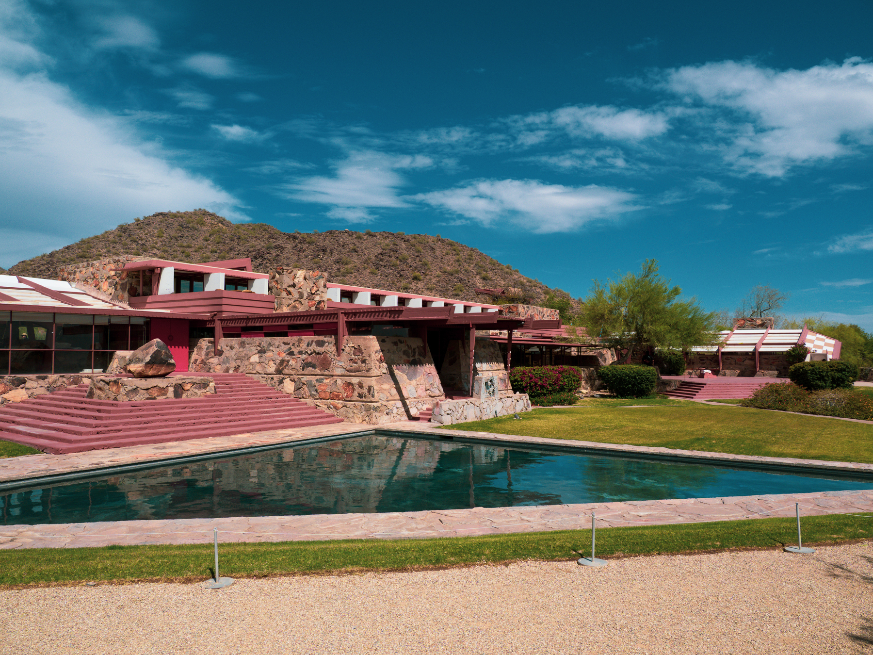 Auto-generated description: A modern architectural complex with linear structures and a reflective pool sits against a backdrop of hills and a partly cloudy sky.