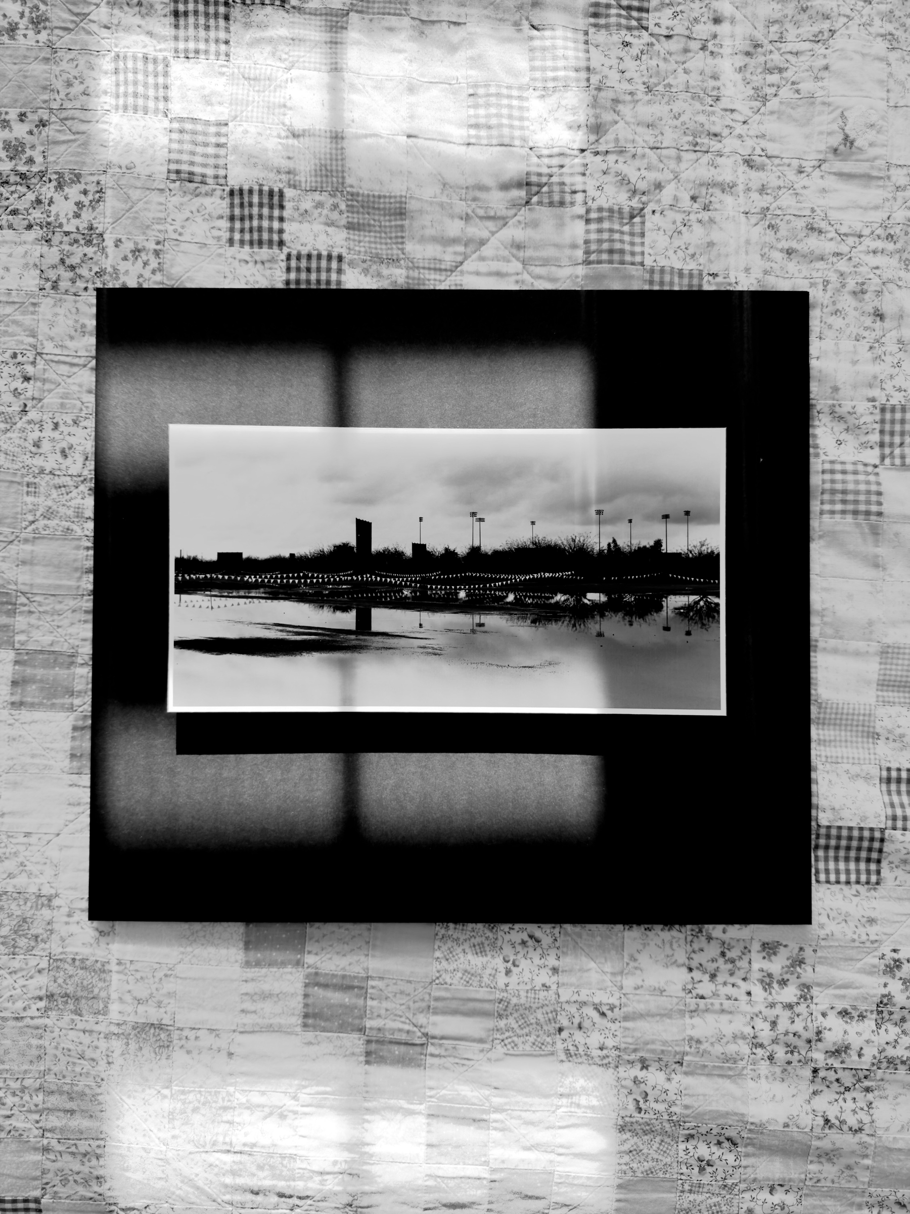 Auto-generated description: A black and white photo of a cityscape with a reflected skyline is framed and displayed on a patterned wall.