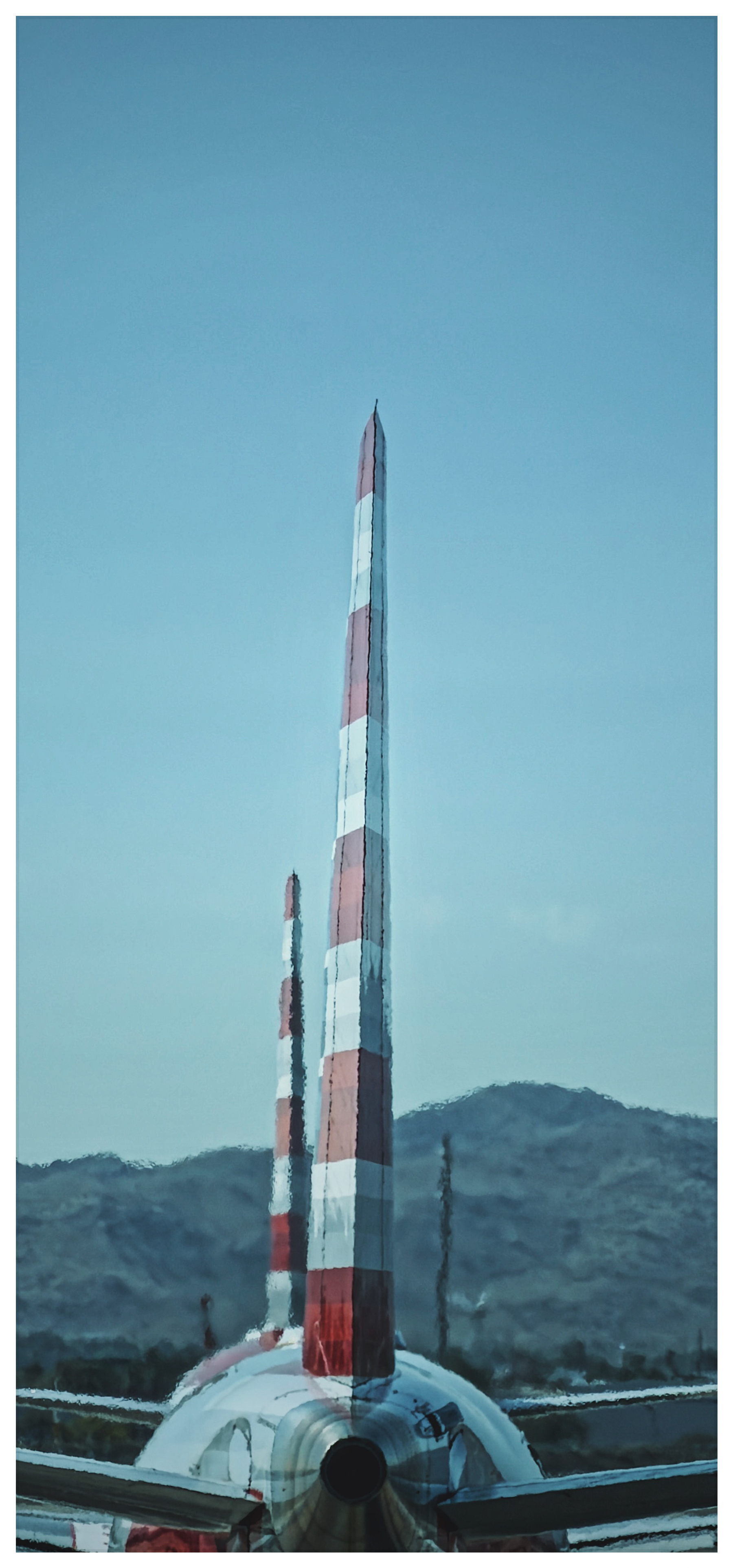 Auto-generated description: Two airplanes with red and white striped tails are lined up against a backdrop of hills and a clear sky.