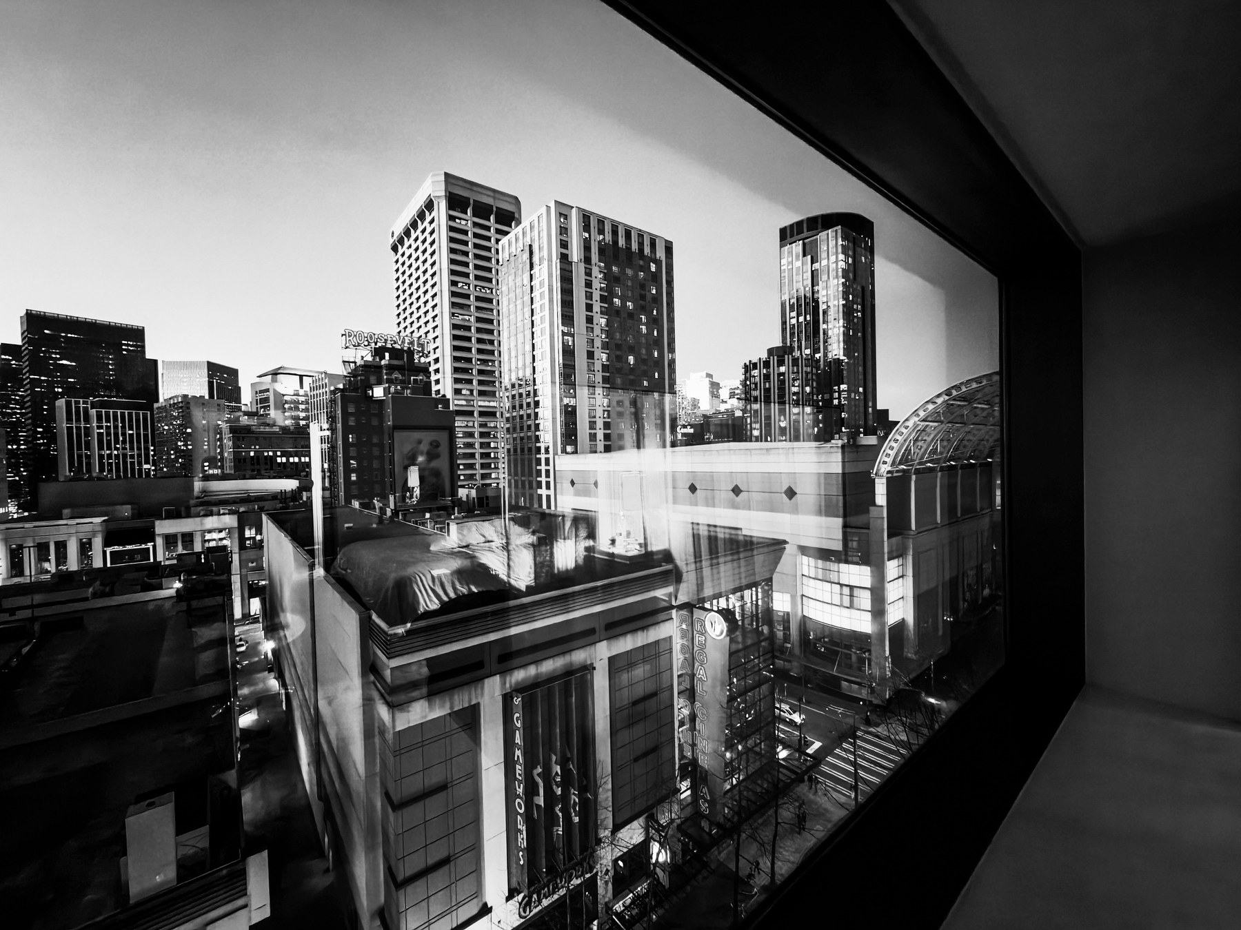 A black and white cityscape view through a window captures a bustling urban skyline with tall buildings and streets below.