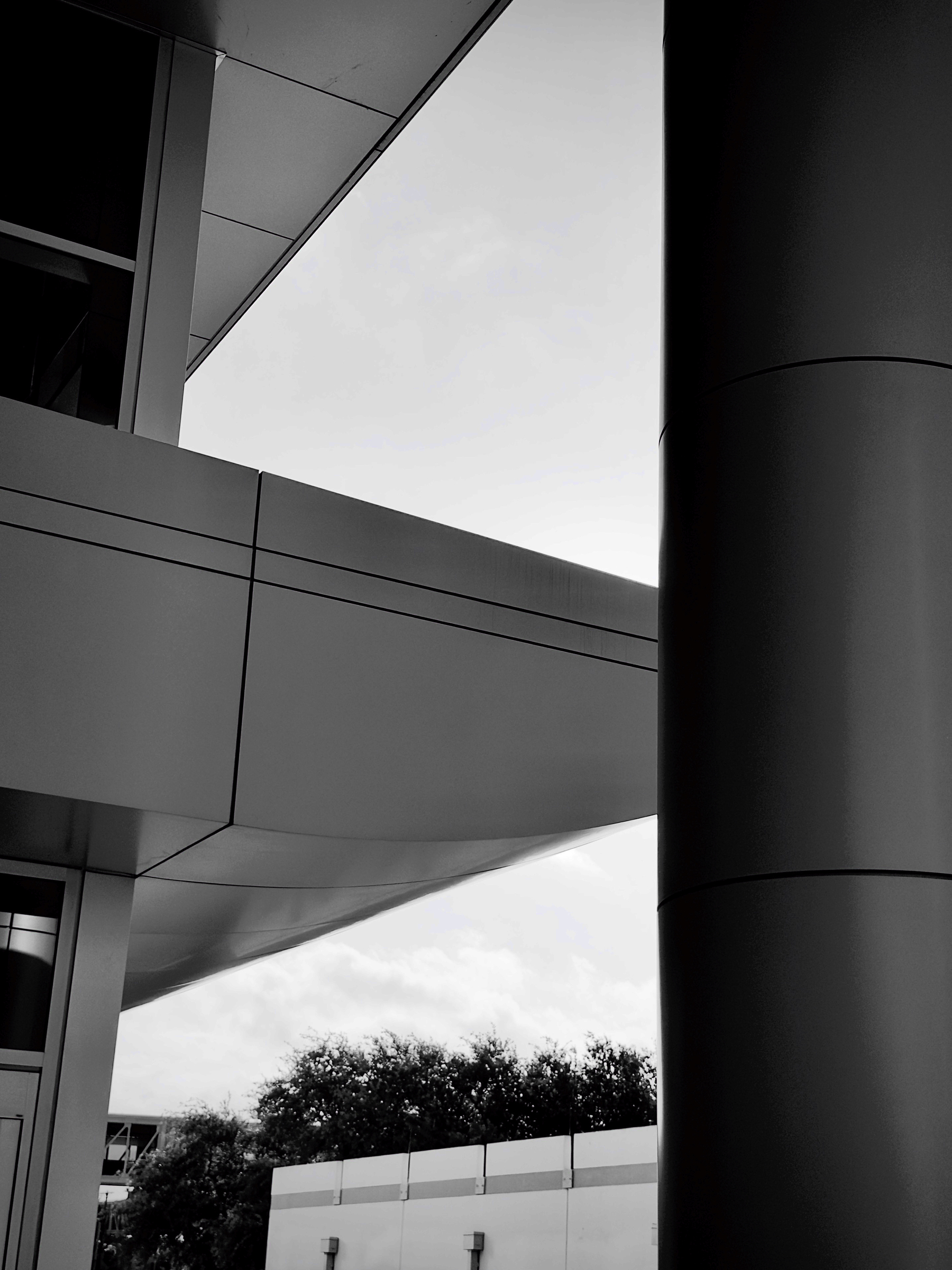 Auto-generated description: A modern architectural structure features sleek geometric lines, a large cylindrical column, and a view of the sky and trees.