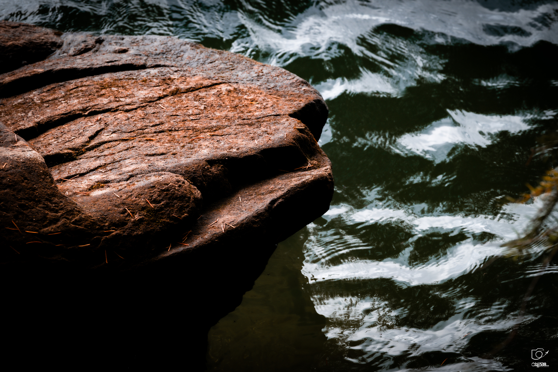 Auto-generated description: A textured reddish-brown rock extends over dark, rippling water.