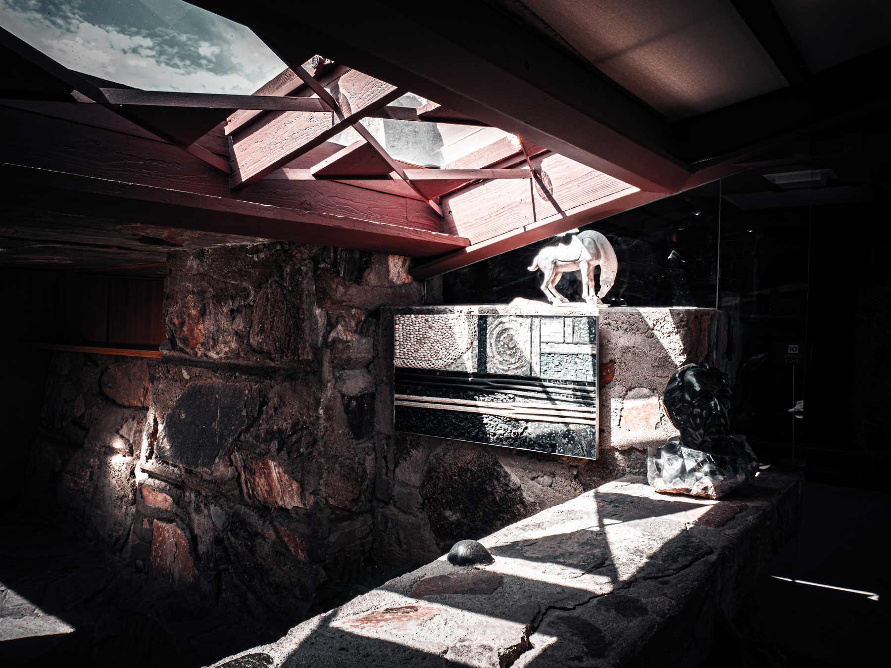 Auto-generated description: Sunlight streams through a skylight, illuminating sculptures and textured stone walls in an architectural space.