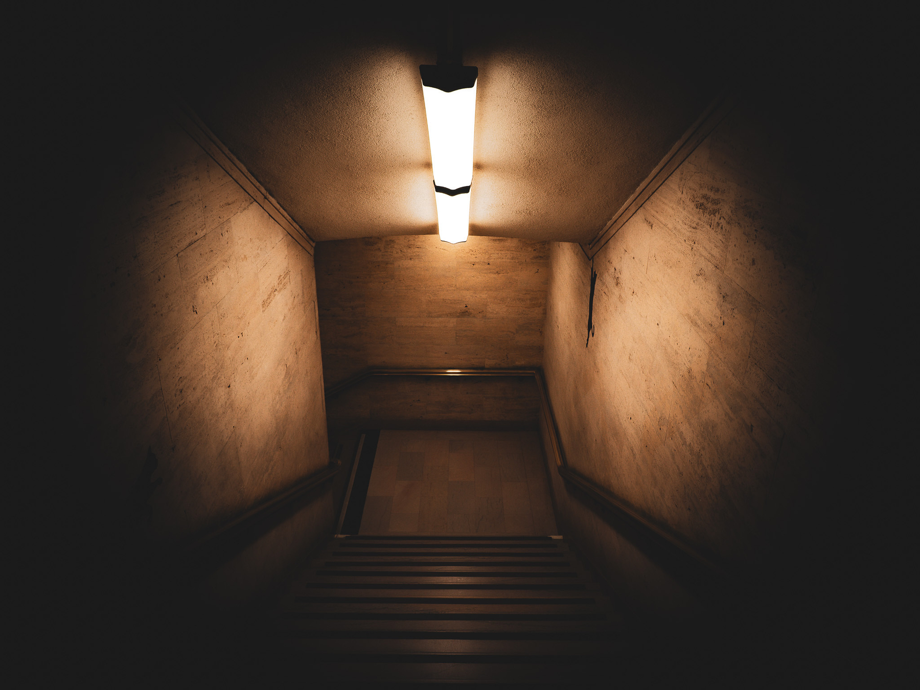 Auto-generated description: A dimly lit staircase leads downward, illuminated by a single overhead light.