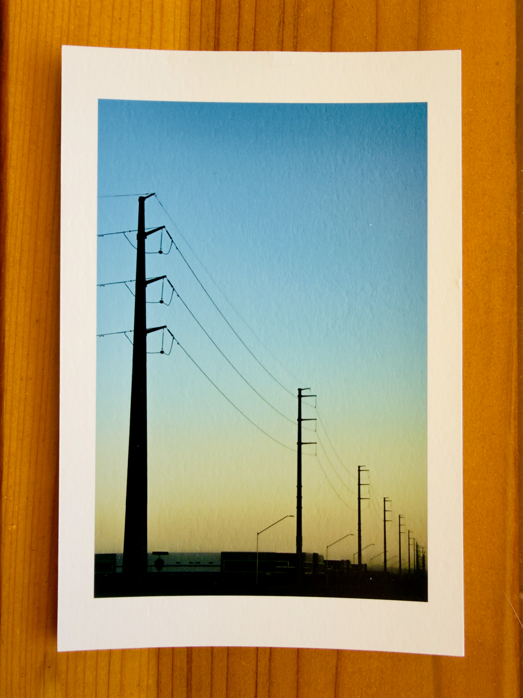 Auto-generated description: A photograph of power lines against a sunset sky is placed on a wooden surface.