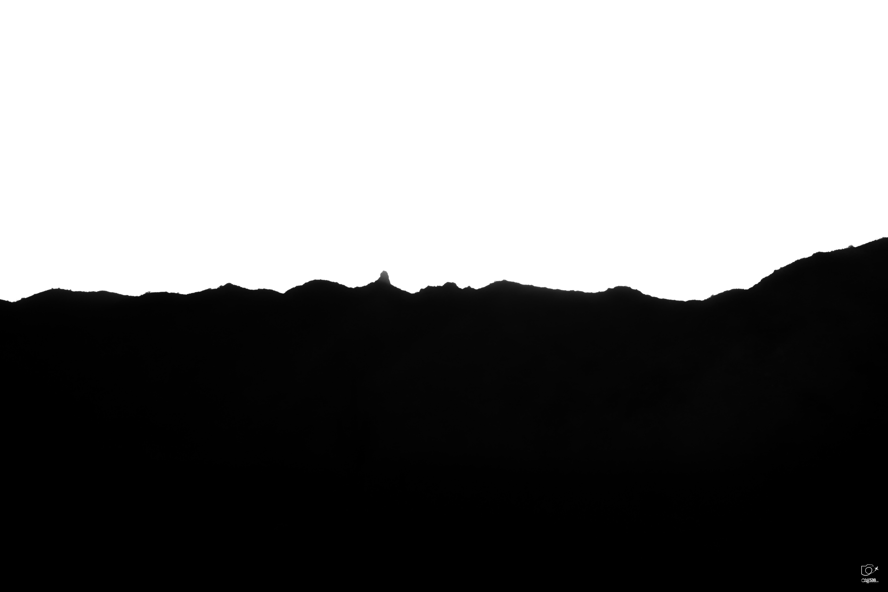 Auto-generated description: A silhouette of a mountain range with a single peak prominently standing out against a clear white sky.