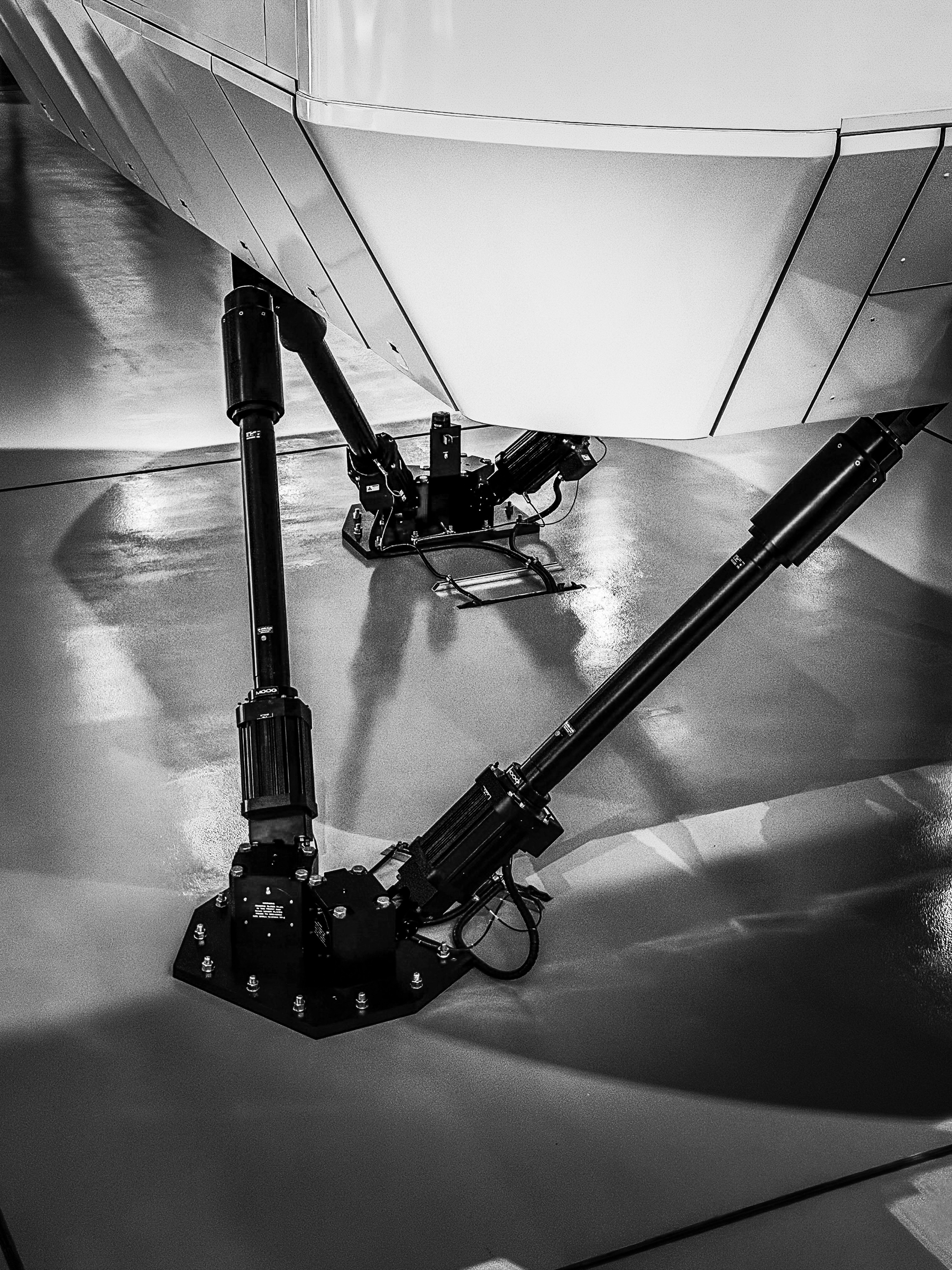 Auto-generated description: A close-up view of three hydraulic pistons attached to a mechanical structure, possibly part of a flight simulator or industrial machinery.