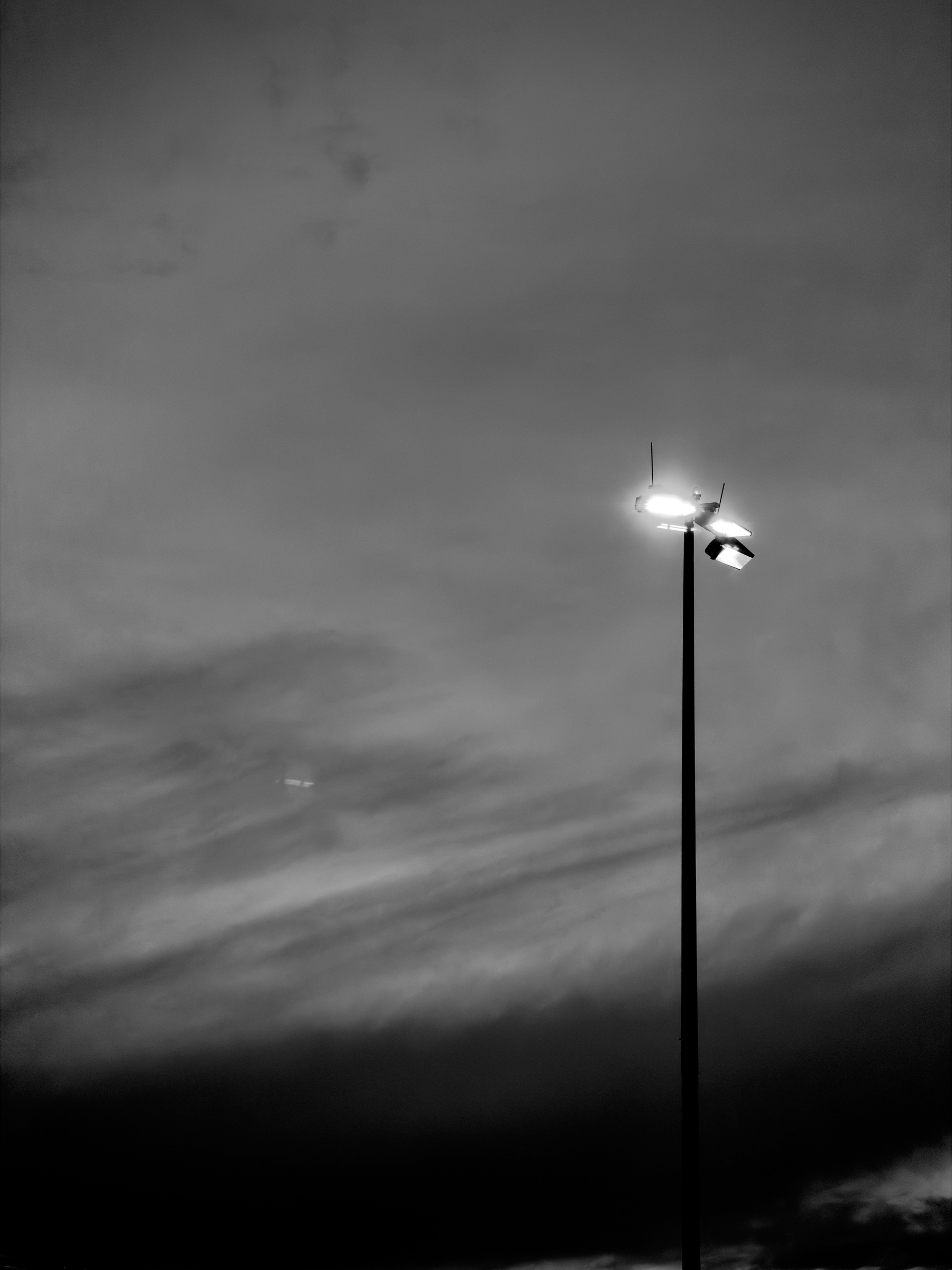 Auto-generated description: A tall streetlight is illuminated against a dark, cloudy sky at dusk or night.