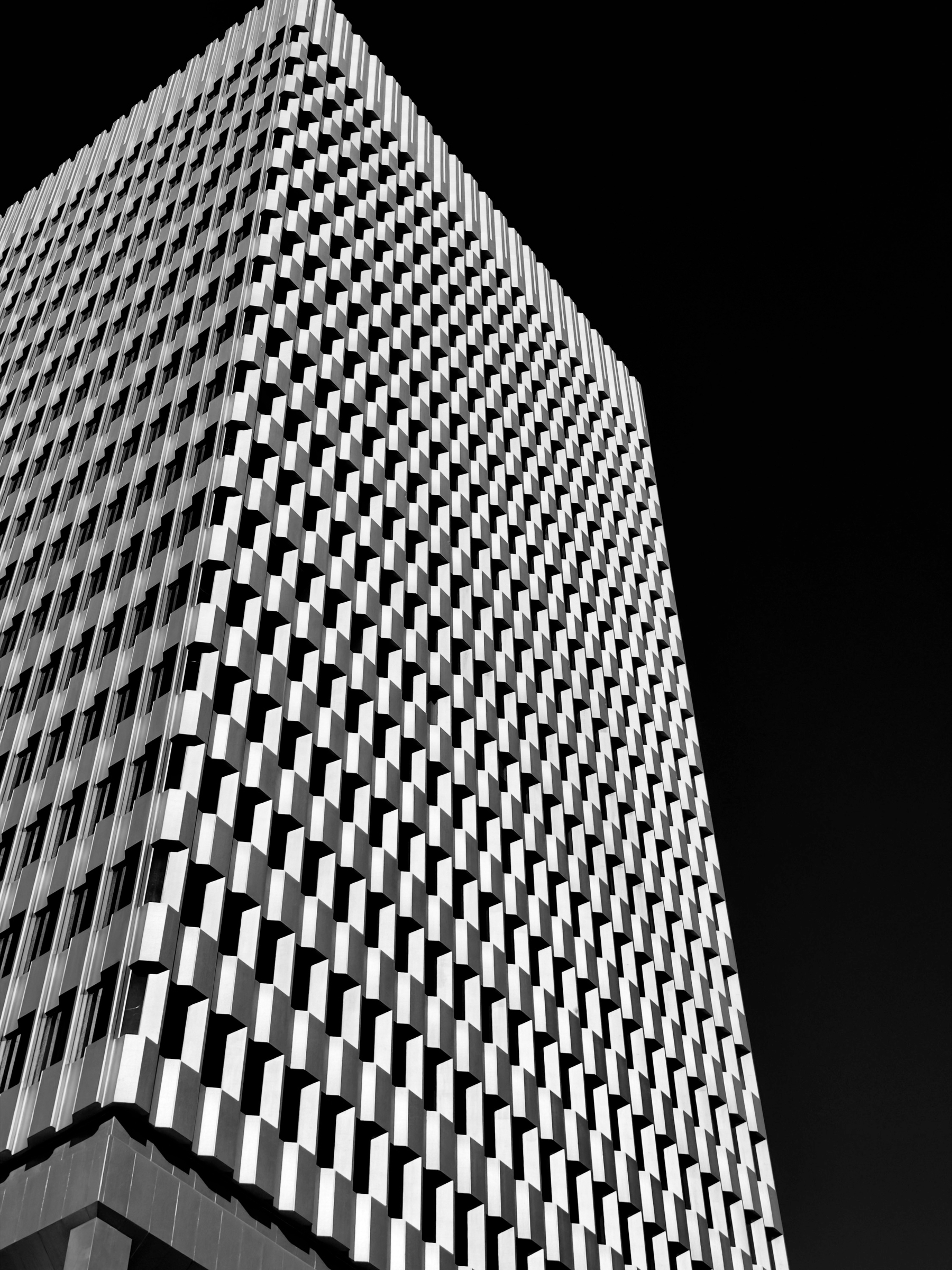 Auto-generated description: A high-rise building featuring a grid-like facade is shown against a stark black sky.