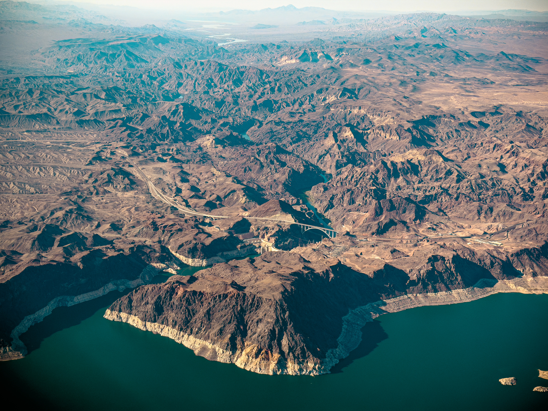 Auto-generated description: An expansive aerial view of a rugged, rocky landscape with winding waterways and a large body of water surrounded by mountainous terrain.