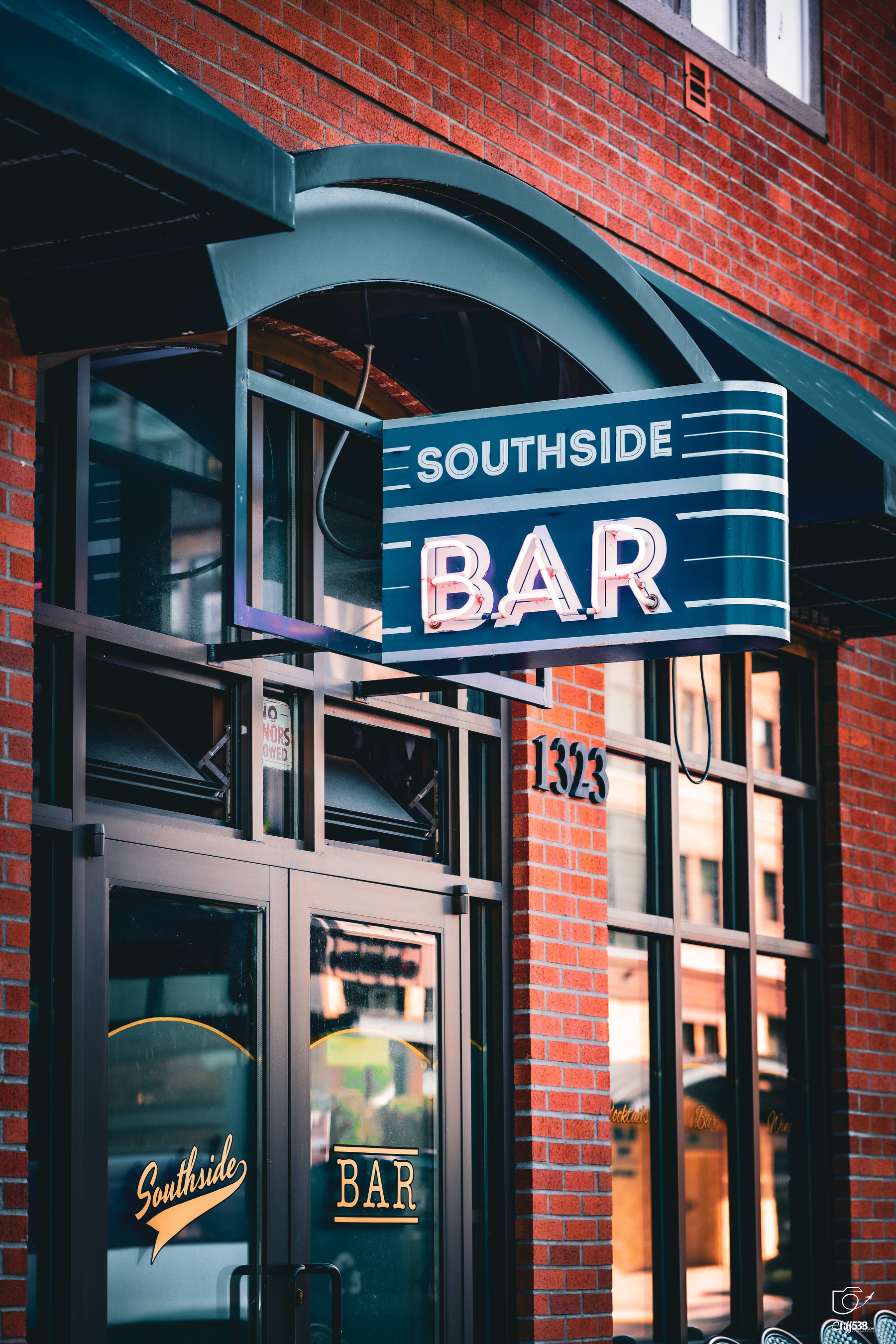 Auto-generated description: A blue and white sign reading Southside Bar hangs above the entrance of a brick building with the address number 1323.