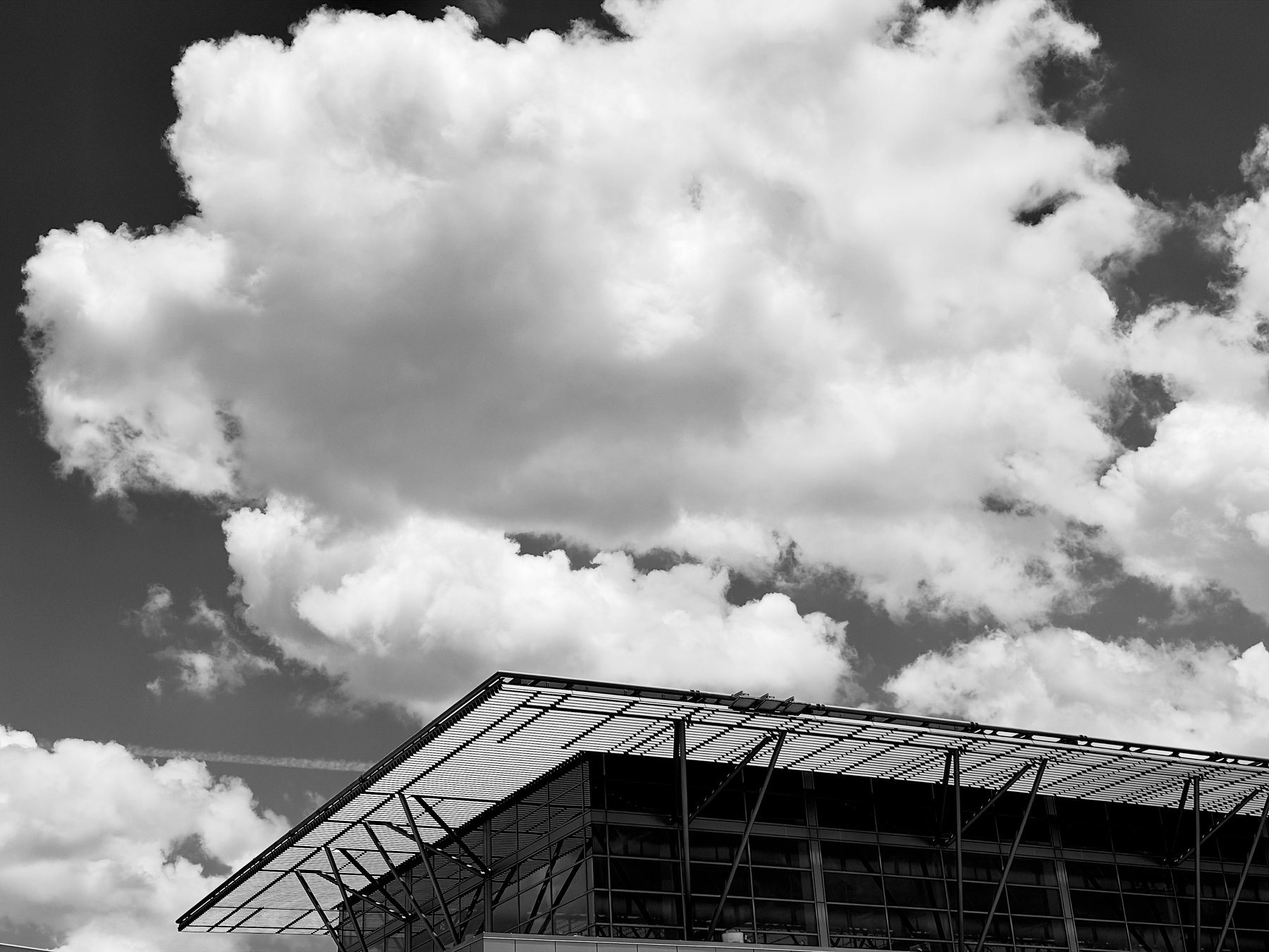 Auto-generated description: A modern building with a slanted roof is set against a backdrop of large, fluffy clouds in the sky.