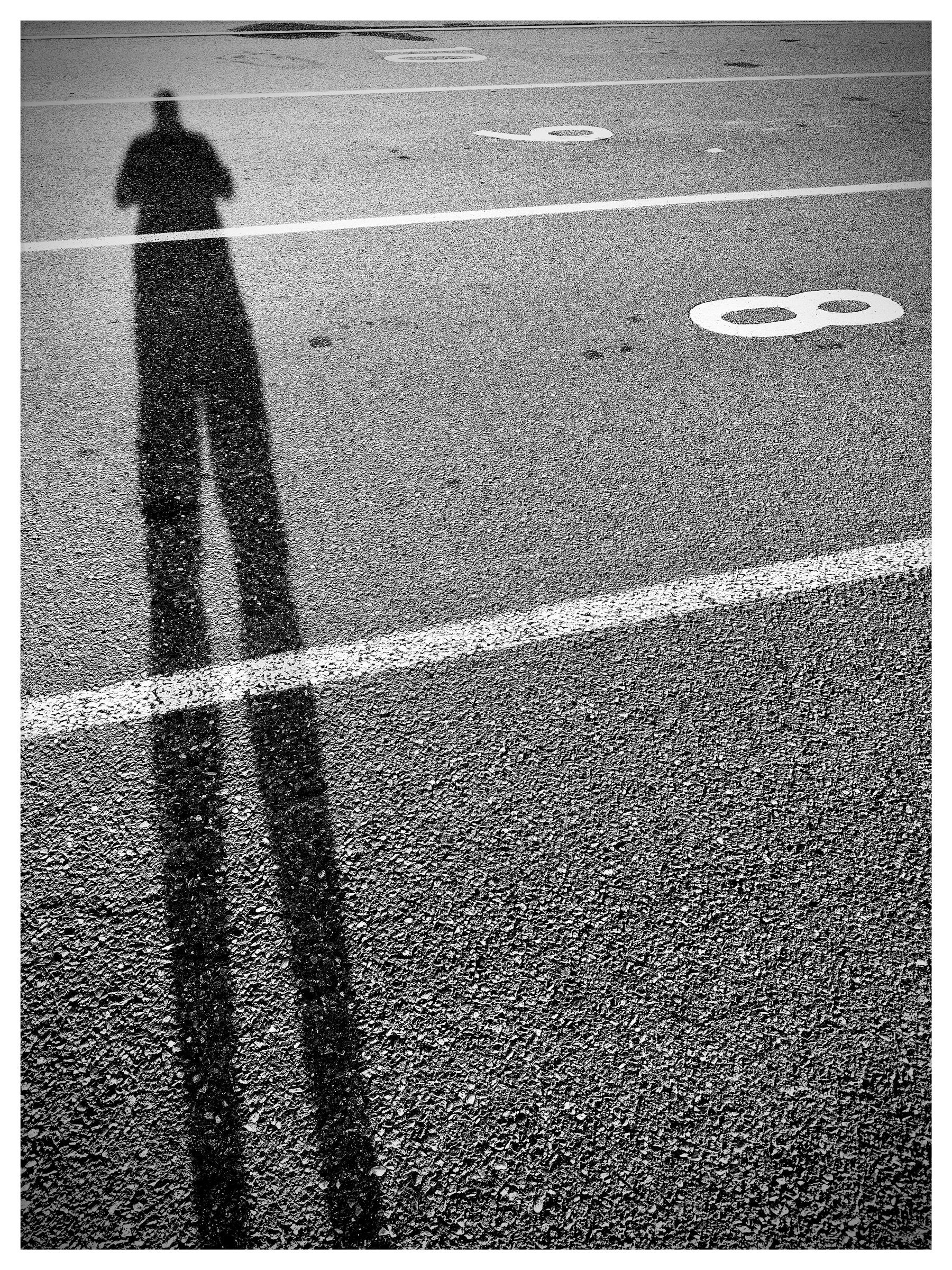 Auto-generated description: A long shadow of a person is cast on a numbered parking lot pavement.