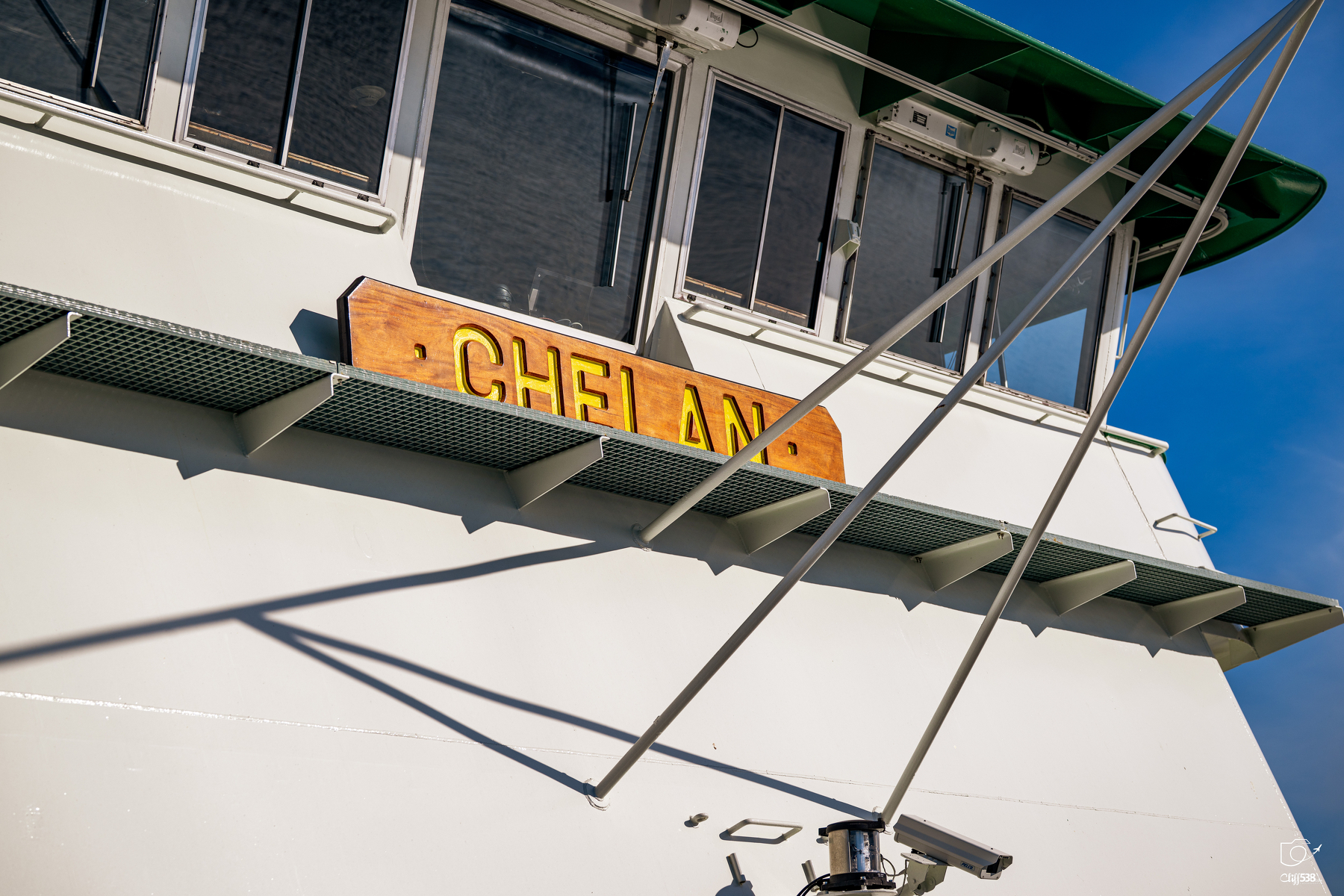 Auto-generated description: The side of a white boat named Chelan is shown with windows and metal beams extending outward.