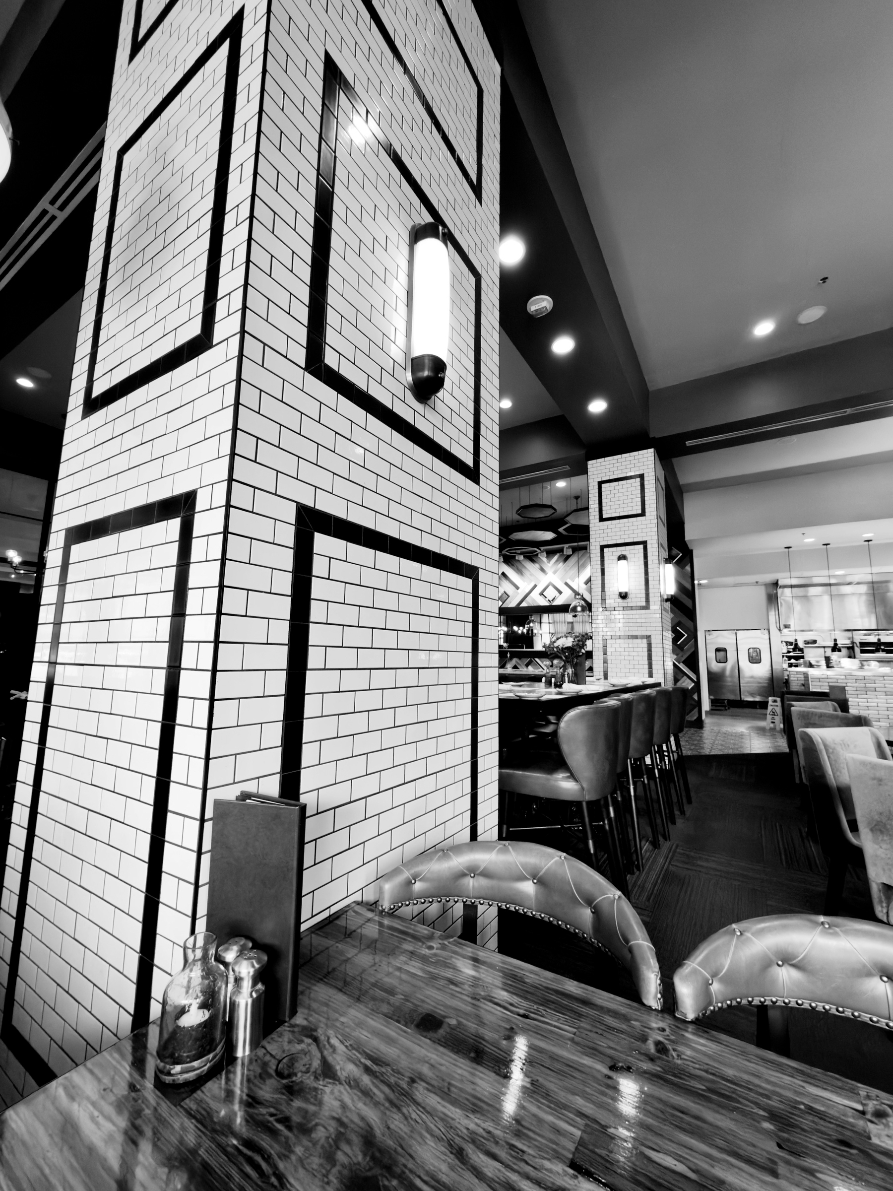 Auto-generated description: A modern dining area features tiled columns with black trim, leather chairs, a wooden table, and ambient lighting.
