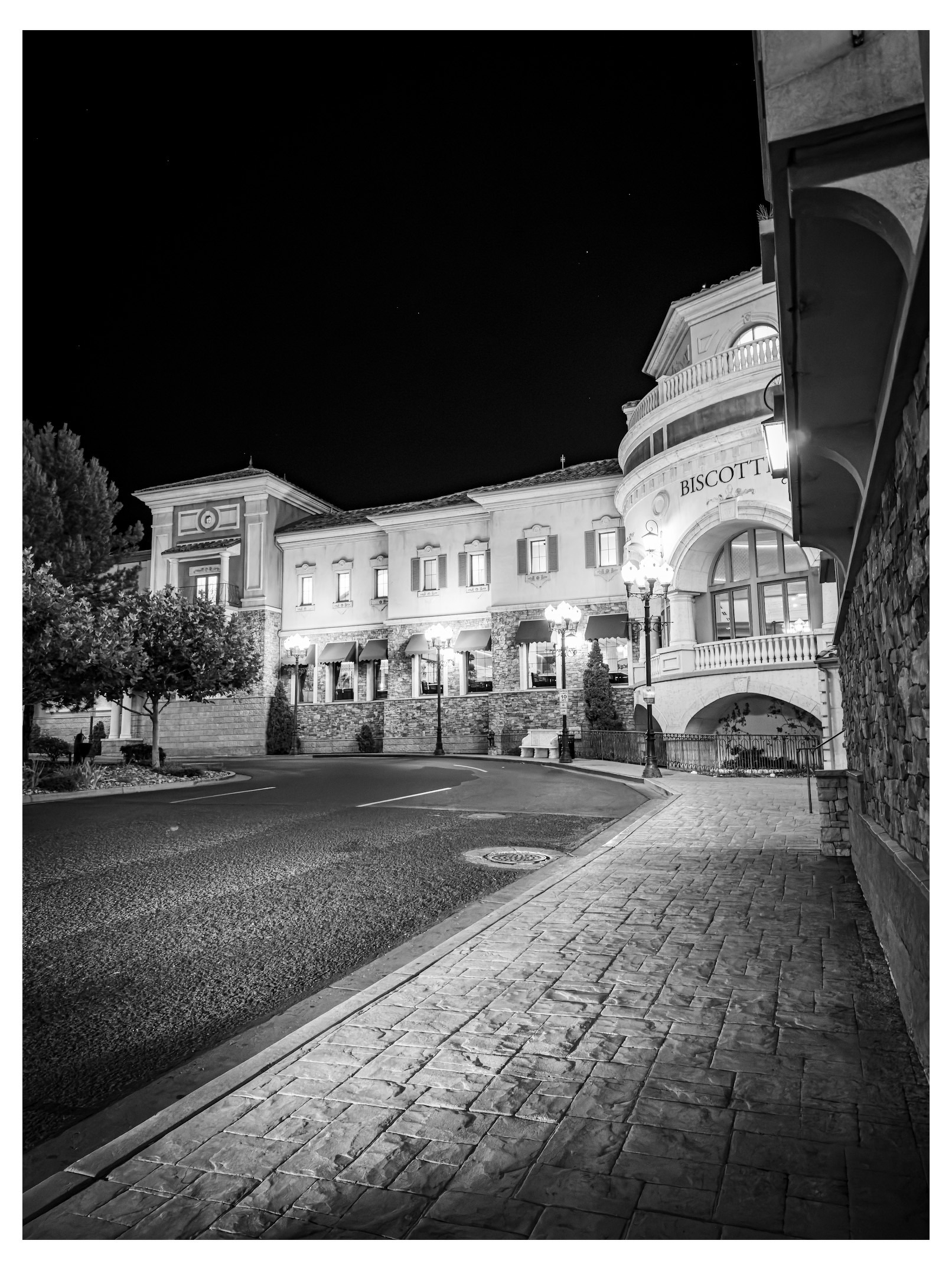 Auto-generated description: A quiet, well-lit street at night features a large, elegant building with architectural details and the word BISCOTTI on a rounded section.