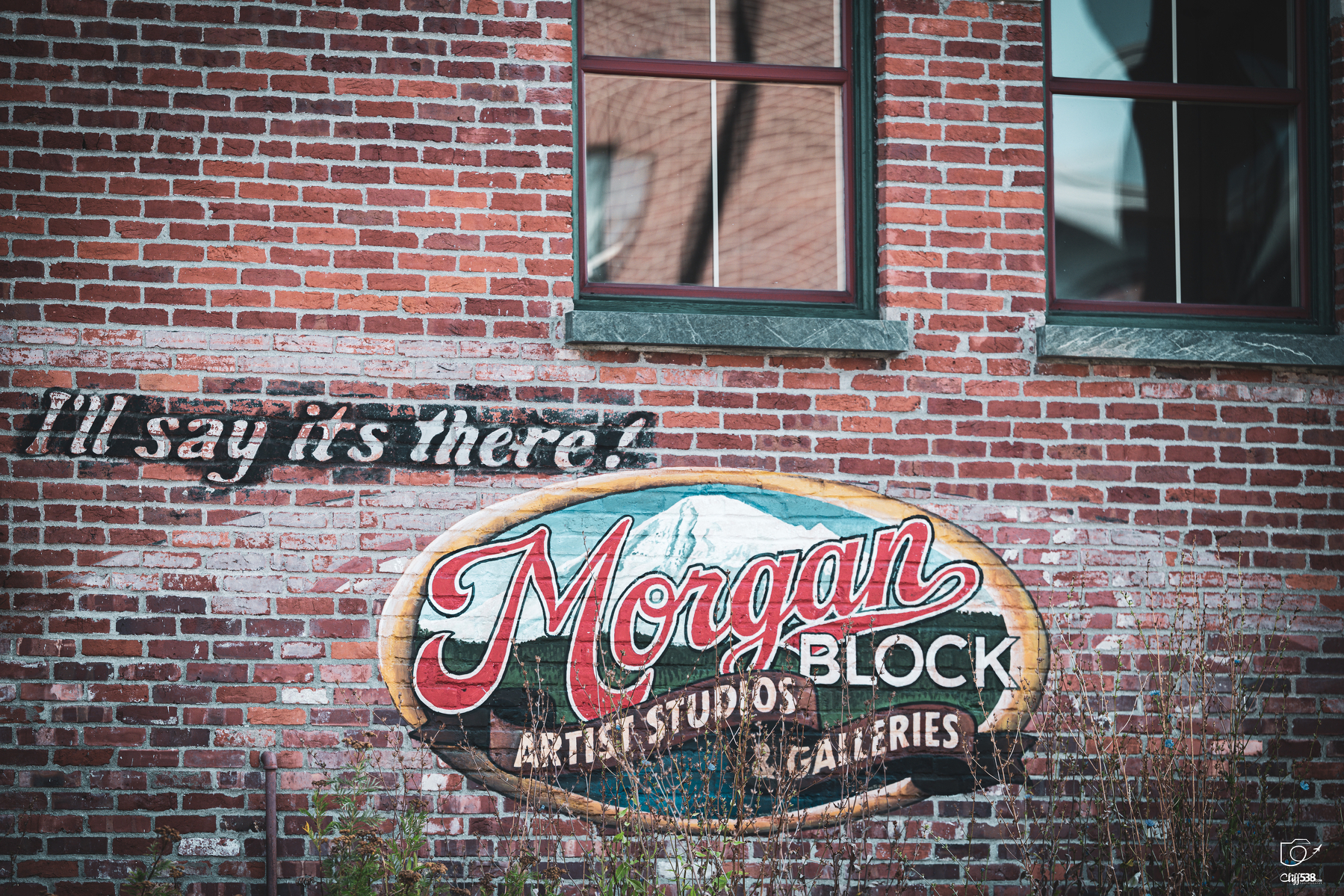 Auto-generated description: A painted sign on a brick wall reads Morgan Block Artist Studios Galleries alongside the phrase I'll say it's there! in a cursive font.
