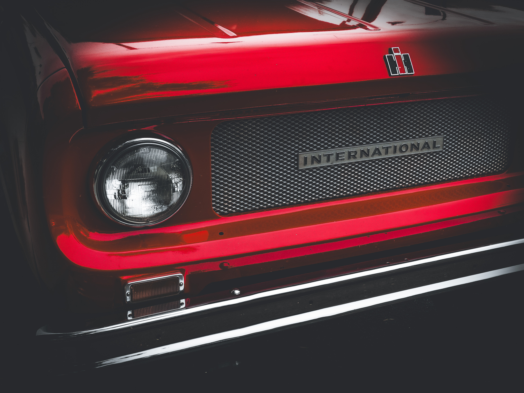 A close-up of the front of a vintage red International Harvester vehicle, featuring its emblem and grille.