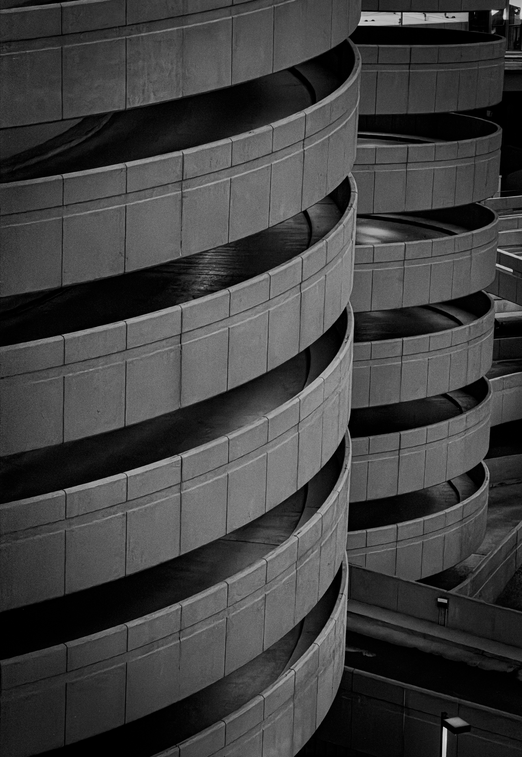 Auto-generated description: Curved, multi-level concrete ramps of a parking garage are shown in a black and white photograph.