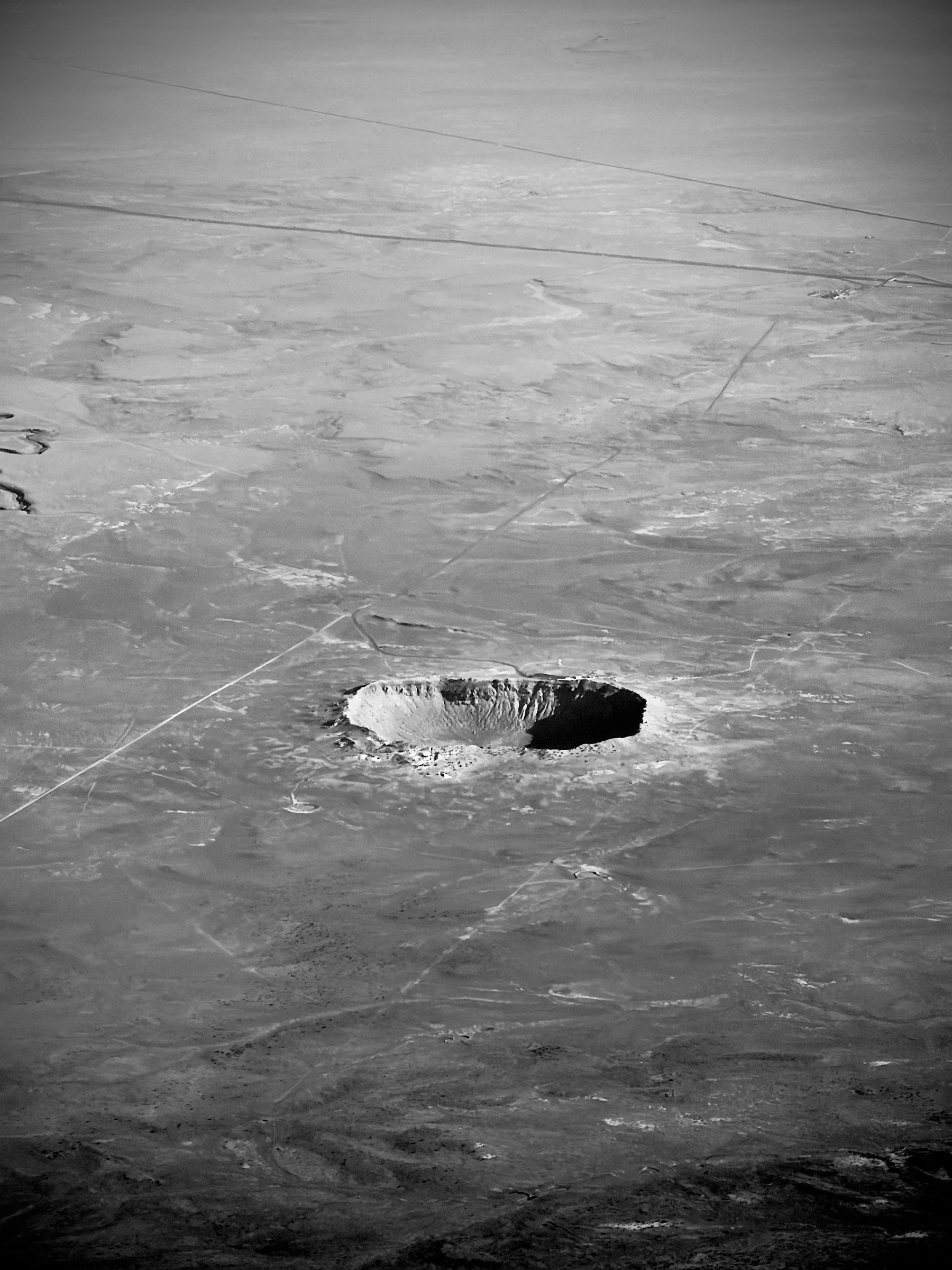 Auto-generated description: A large, circular crater is situated in the middle of an expansive, barren landscape.