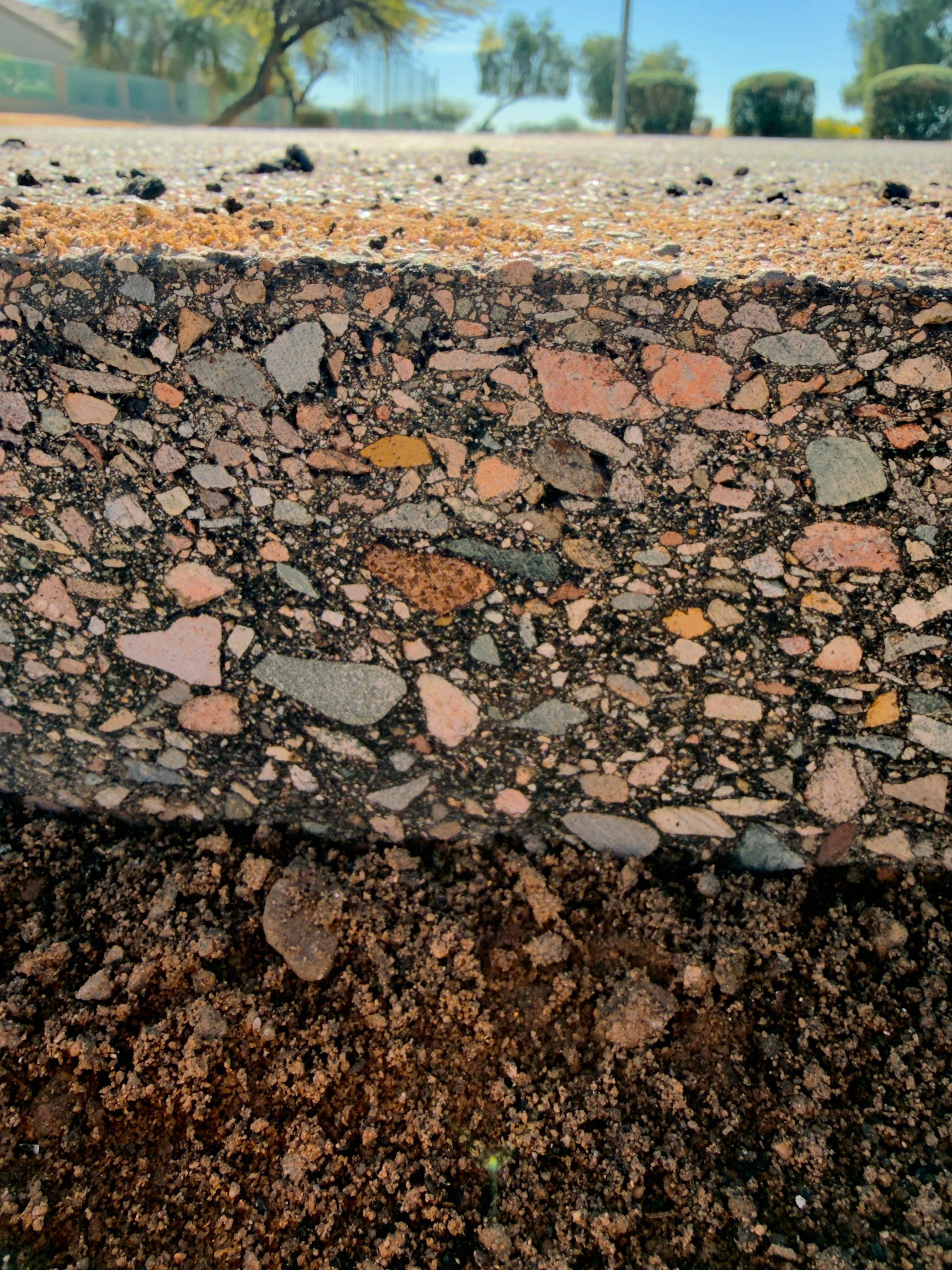 Auto-generated description: A close-up of a cross-section of asphalt pavement reveals a layer of compacted gravel and stone, with soil visible beneath.