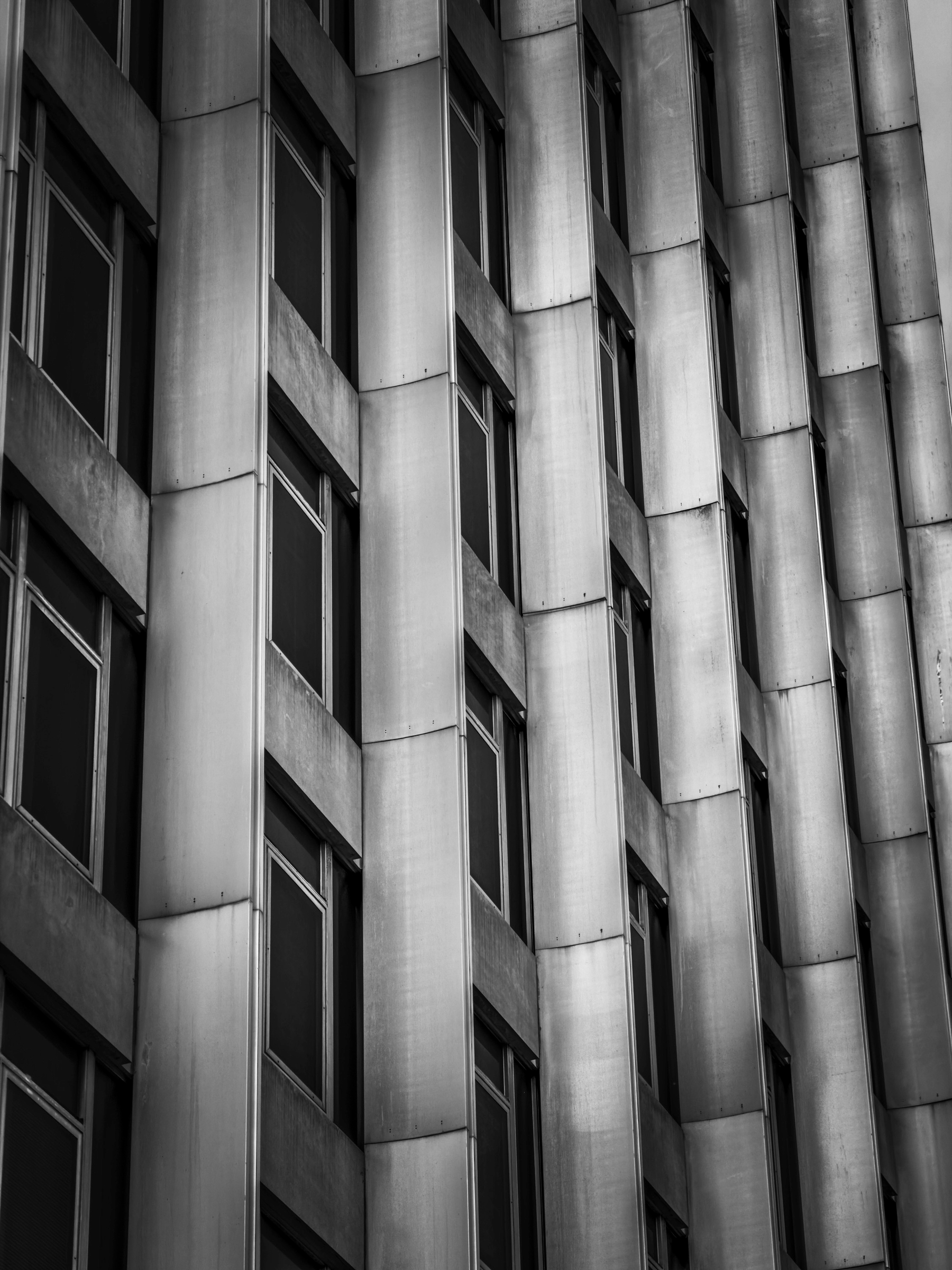 Auto-generated description: A black and white photograph of a high-rise building's exterior featuring repetitive window patterns and metallic façade.