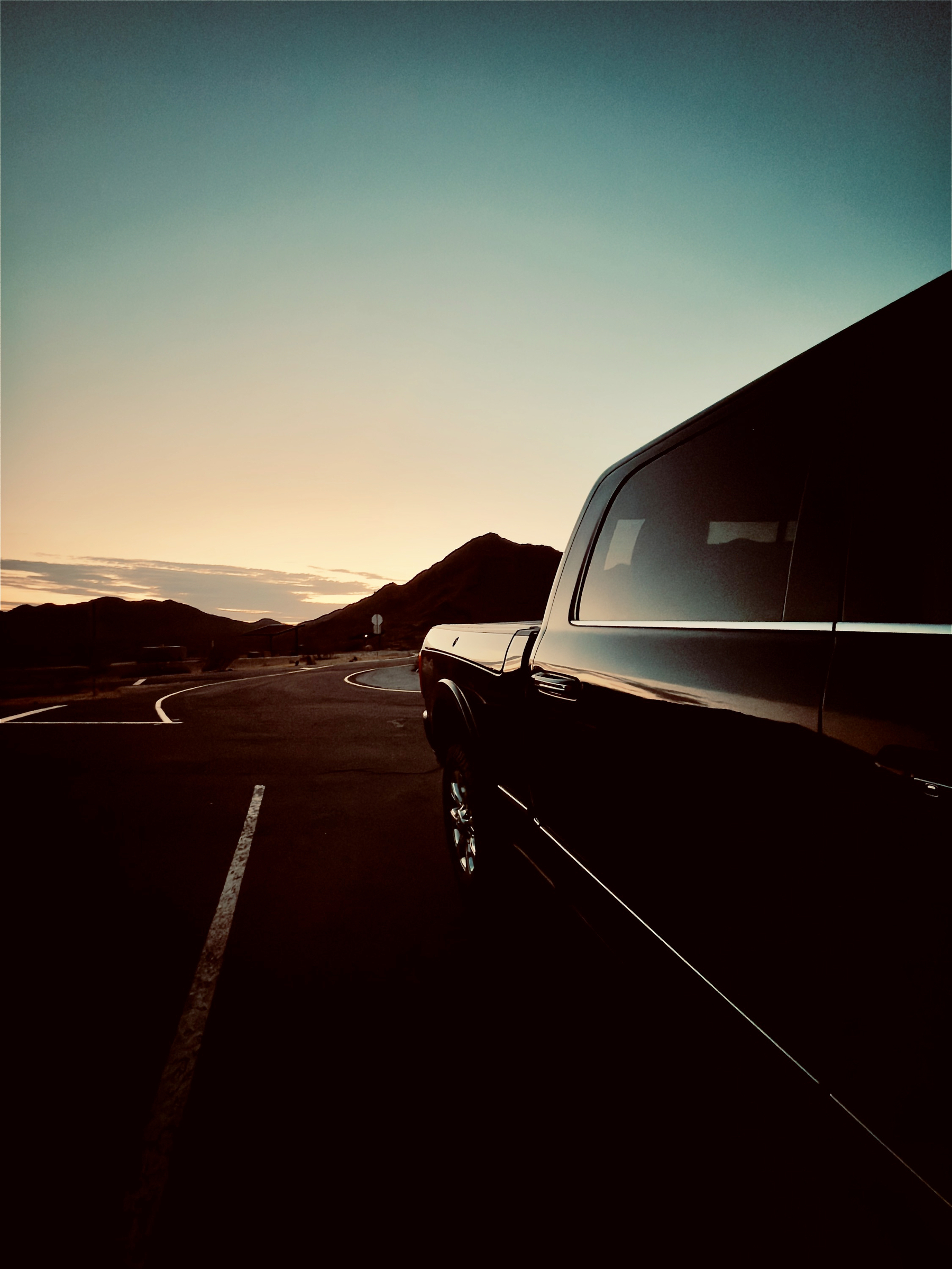 Auto-generated description: A black vehicle is parked on an empty road at sunset with mountains visible in the background.