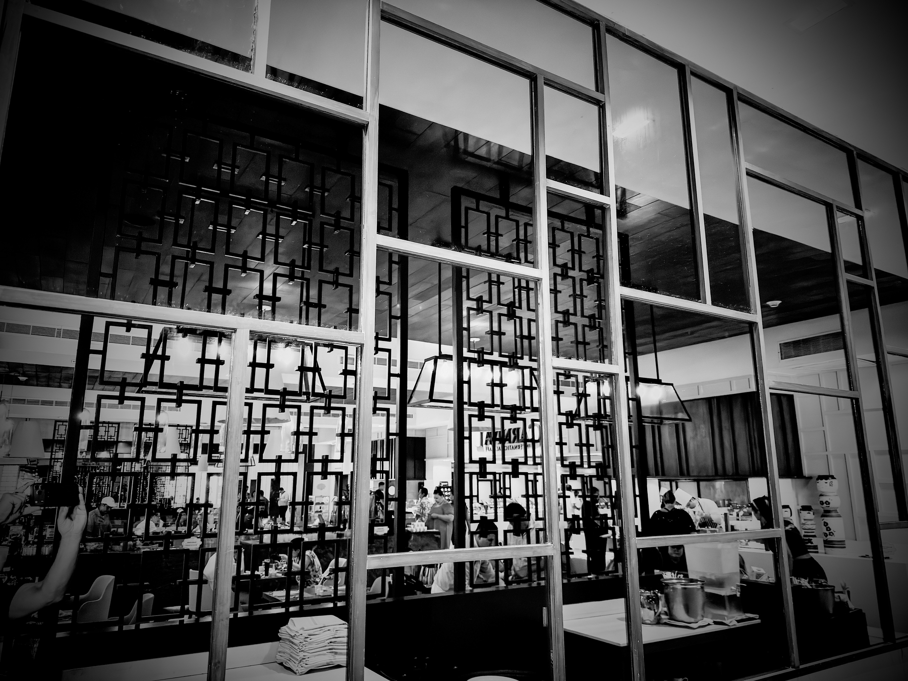 A restaurant interior features decorative geometric wall dividers and people dining in a stylish setting.