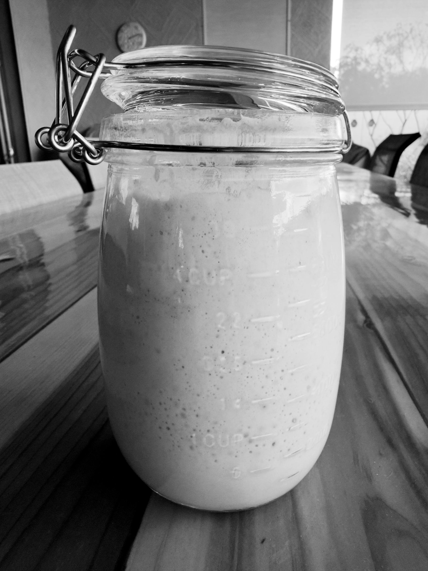 Auto-generated description: A glass jar with a clasp lid is filled with a frothy liquid and placed on a wooden table.