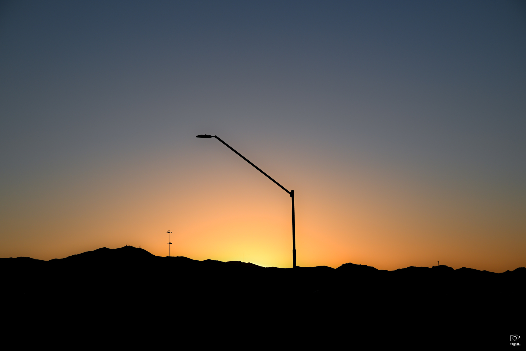 Auto-generated description: A streetlight stands against the backdrop of a vibrant sunset behind distant hills.