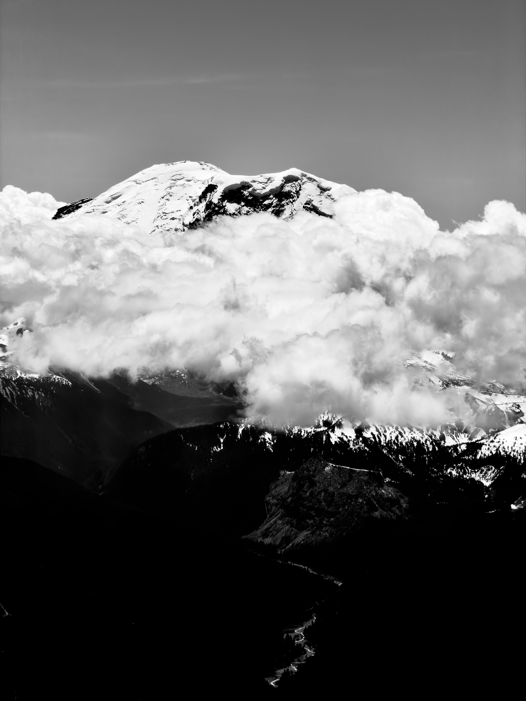 Auto-generated description: A snow-capped mountain peak rises above a layer of clouds with dark, rugged terrain below.