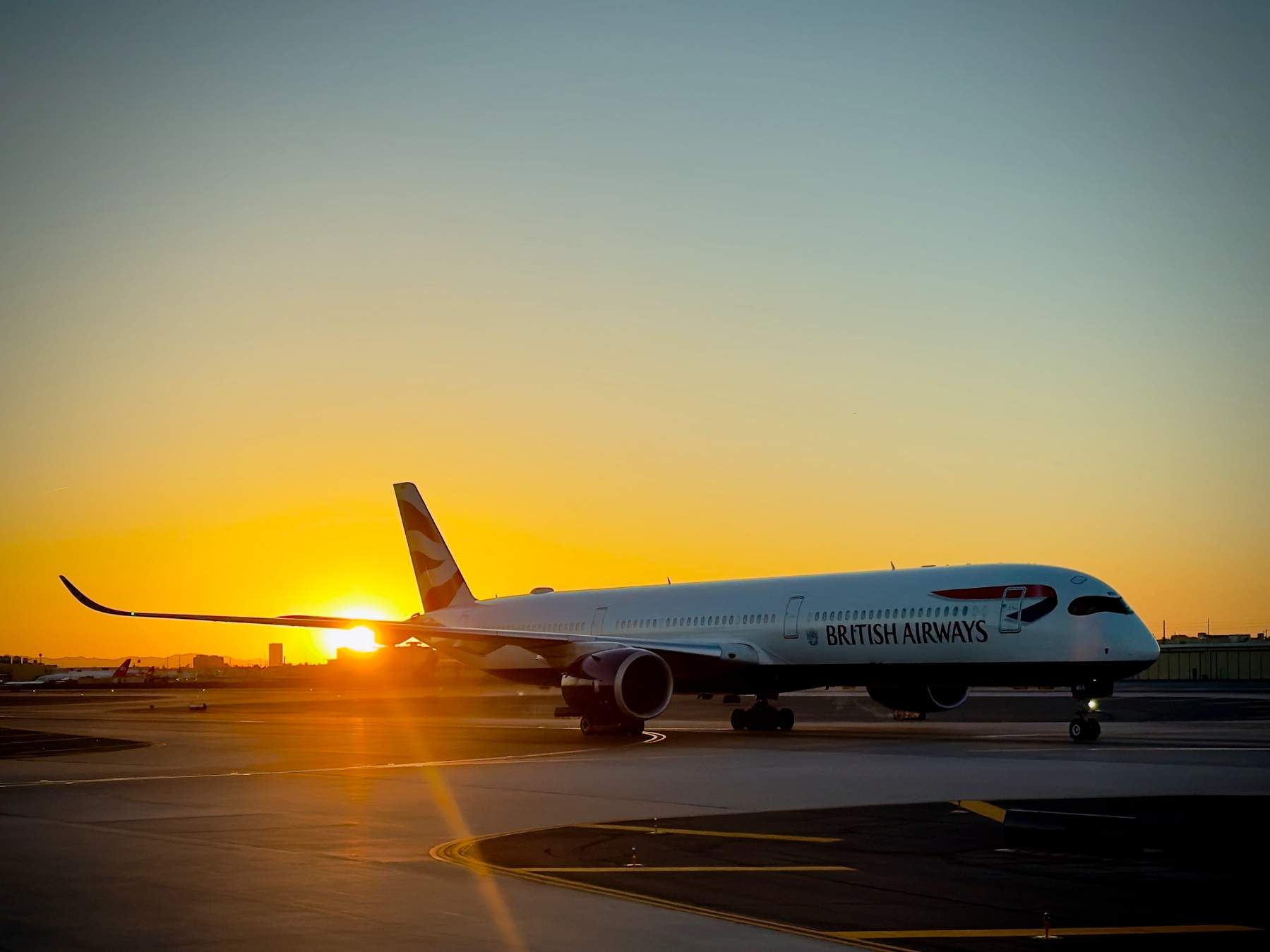 Auto-generated description: A British Airways airplane is taxiing on the runway at sunset.