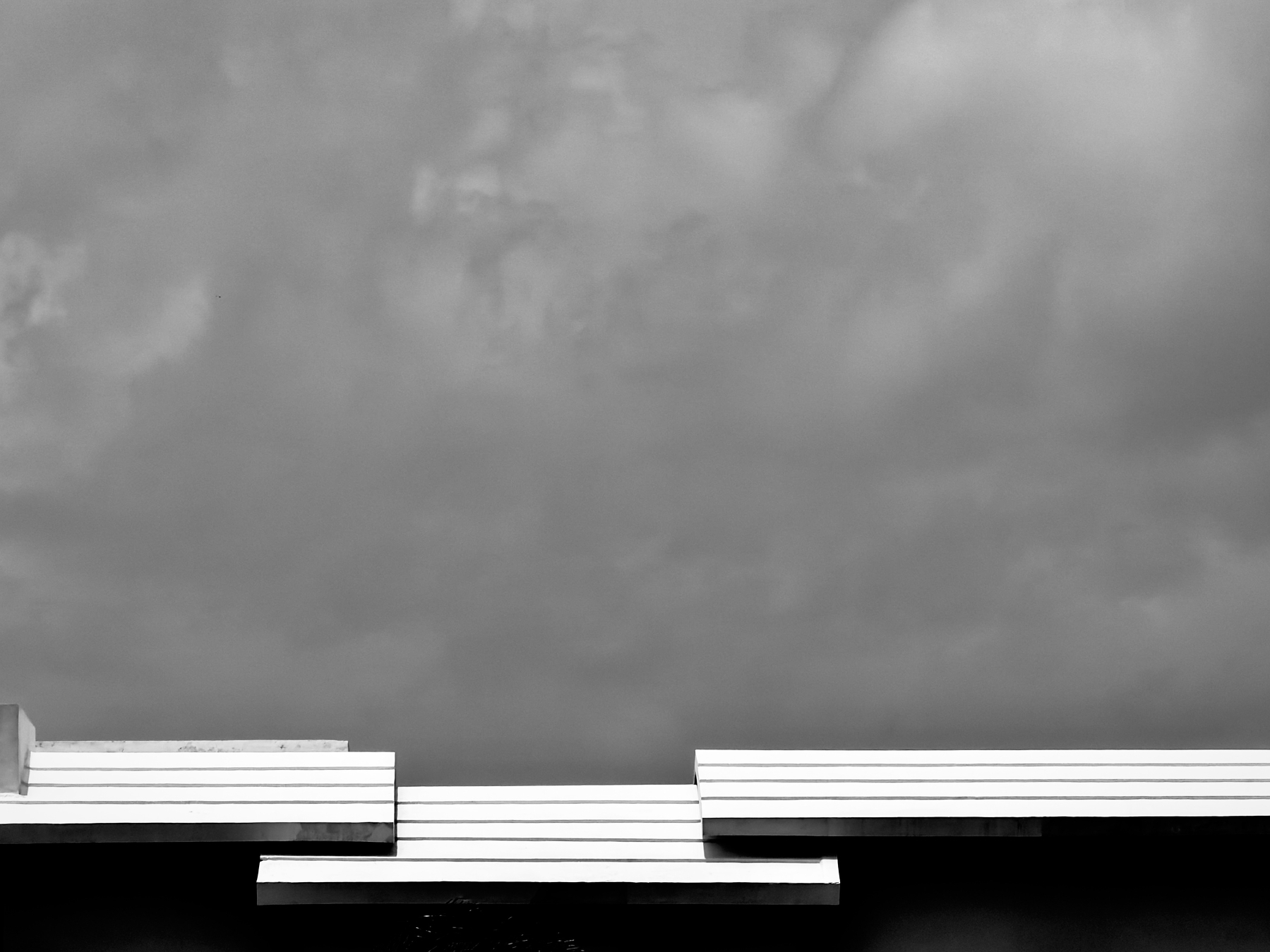 A modern architectural structure with layered horizontal lines is set against a dramatic cloudy sky.