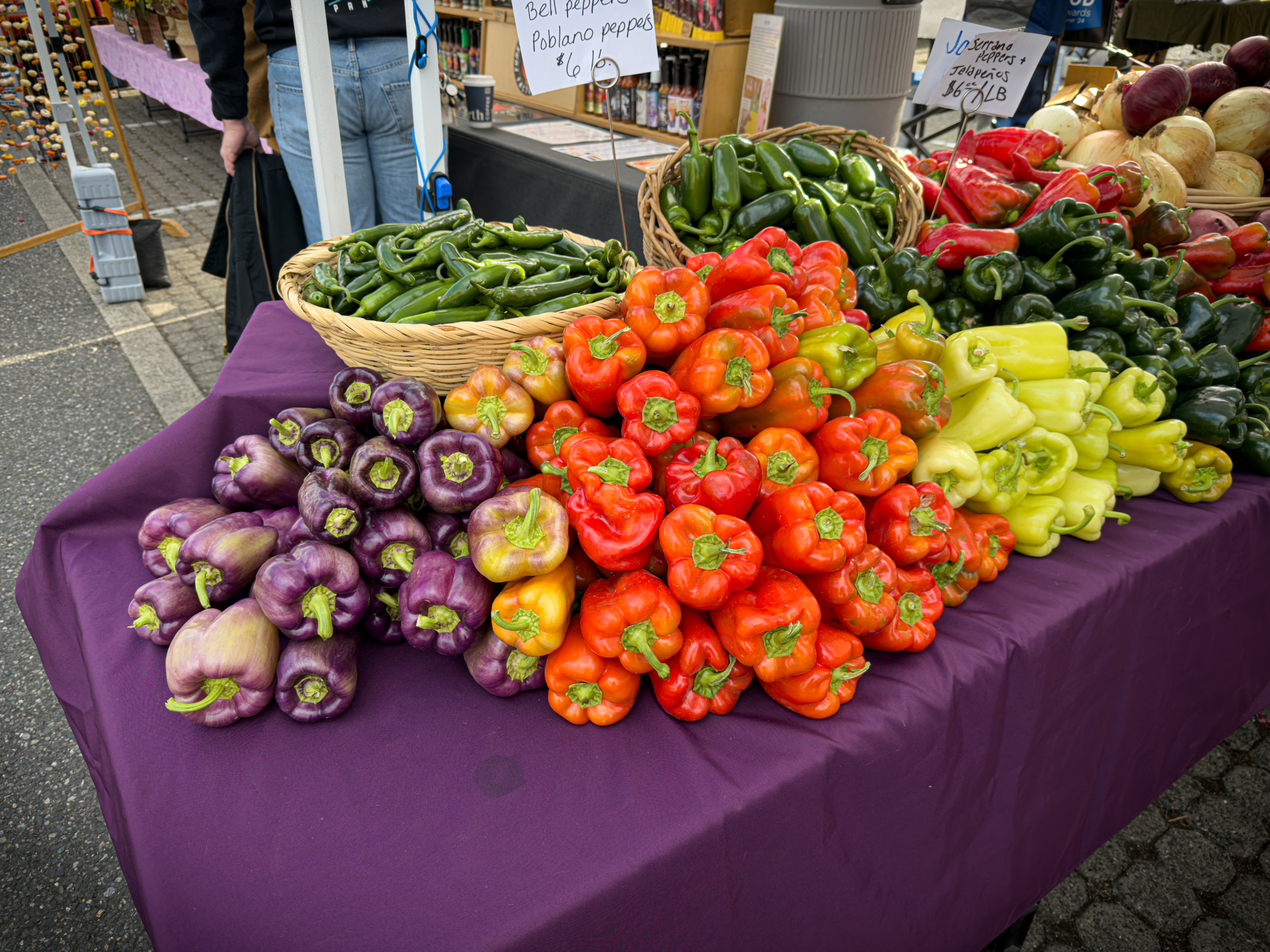 Auto-generated description: A variety of colorful peppers, including purple, red, yellow, and green ones, are neatly arranged on a table covered with a purple cloth at a market stall.