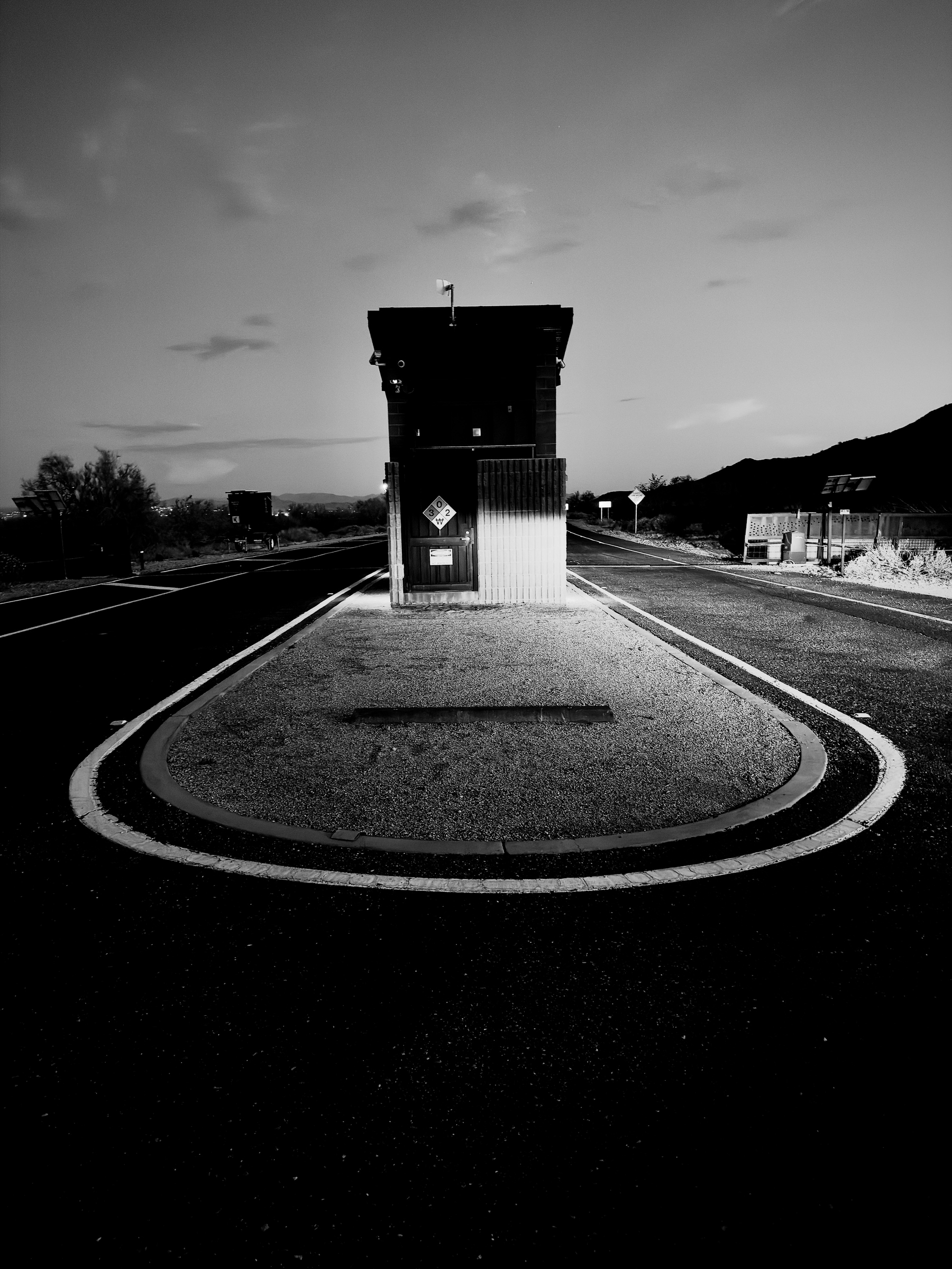 Auto-generated description: A small structure is situated on a raised island between two roads, creating a symmetrical and stark contrast in the black-and-white photograph.