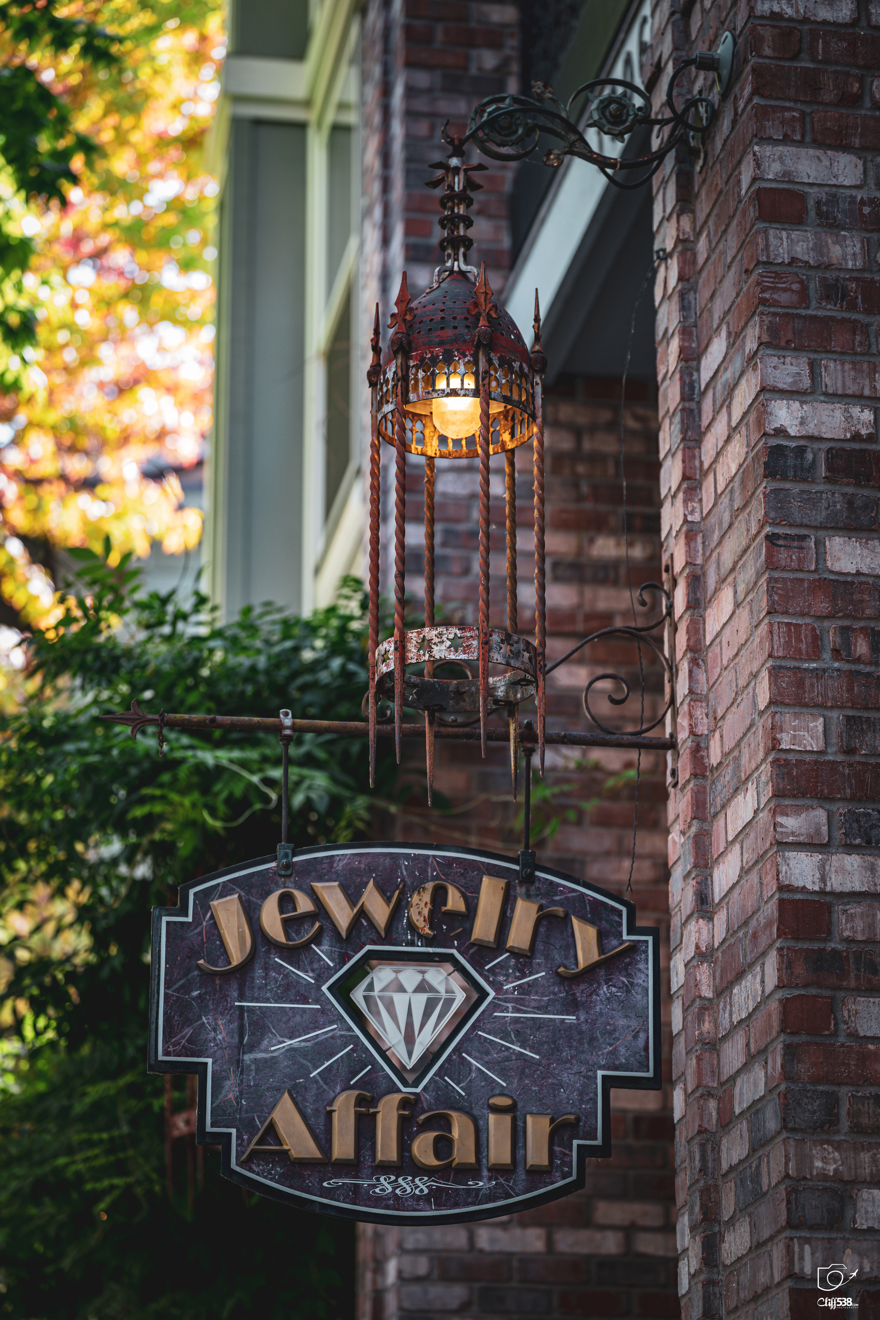 Auto-generated description: A decorative lantern hangs above a sign for a jewelry store named Jewelry Affair attached to a brick wall.