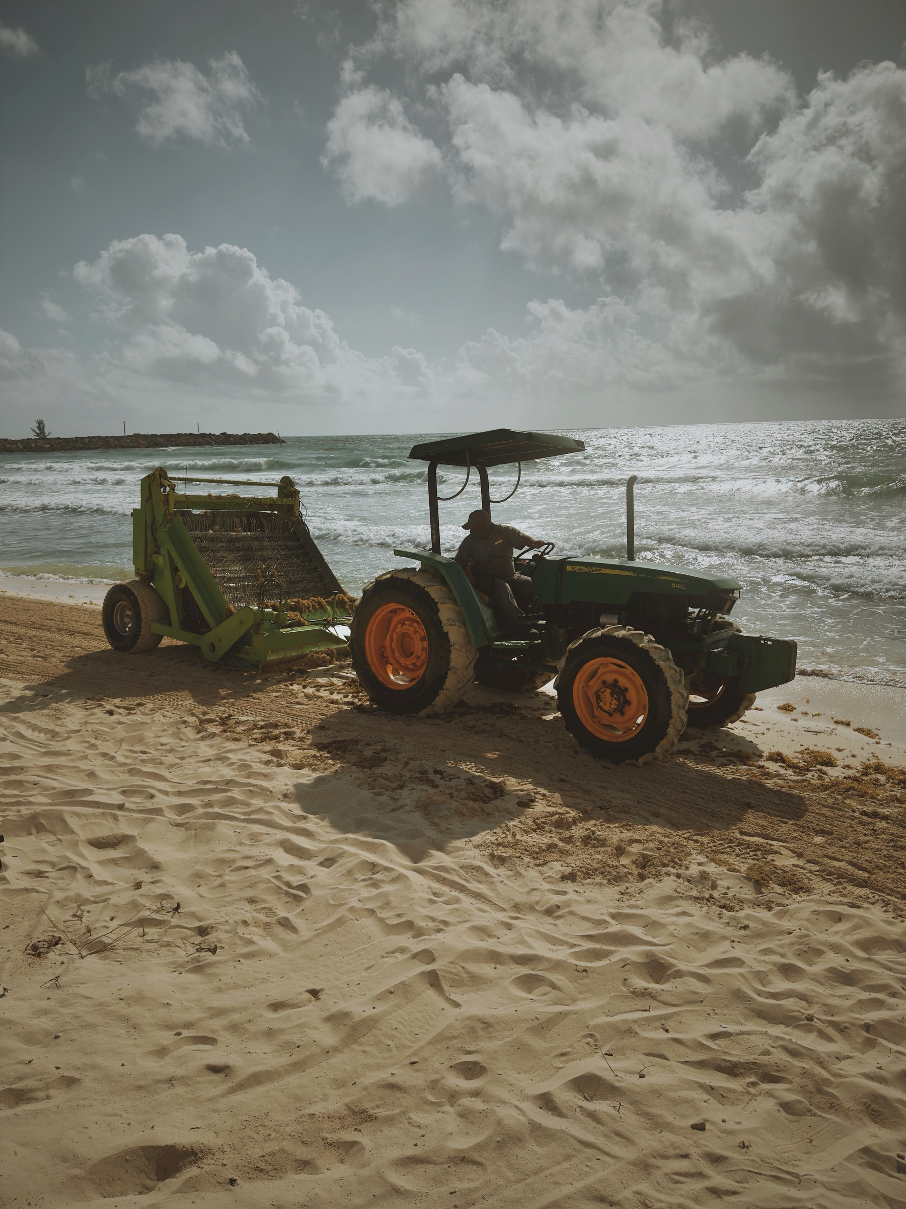 Auto-generated description: A green tractor is parked on a sandy beach near the ocean with a clear blue sky overhead.