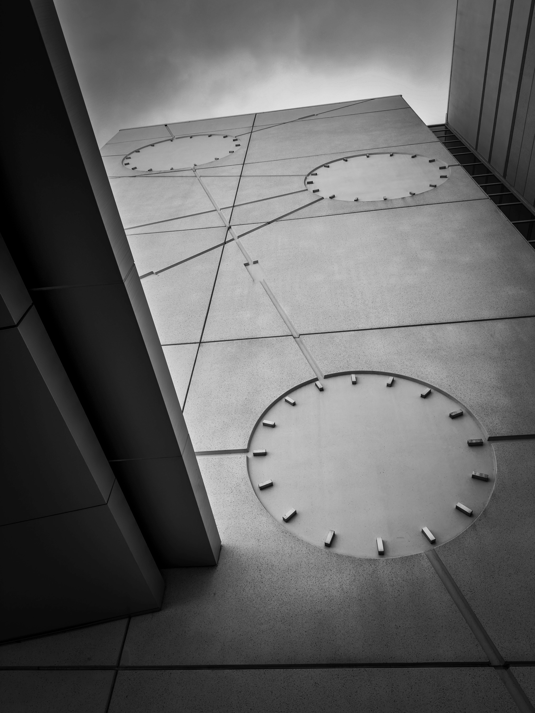 Auto-generated description: A black and white architectural perspective features a modern building facade with circular designs and linear elements against a cloudy sky.