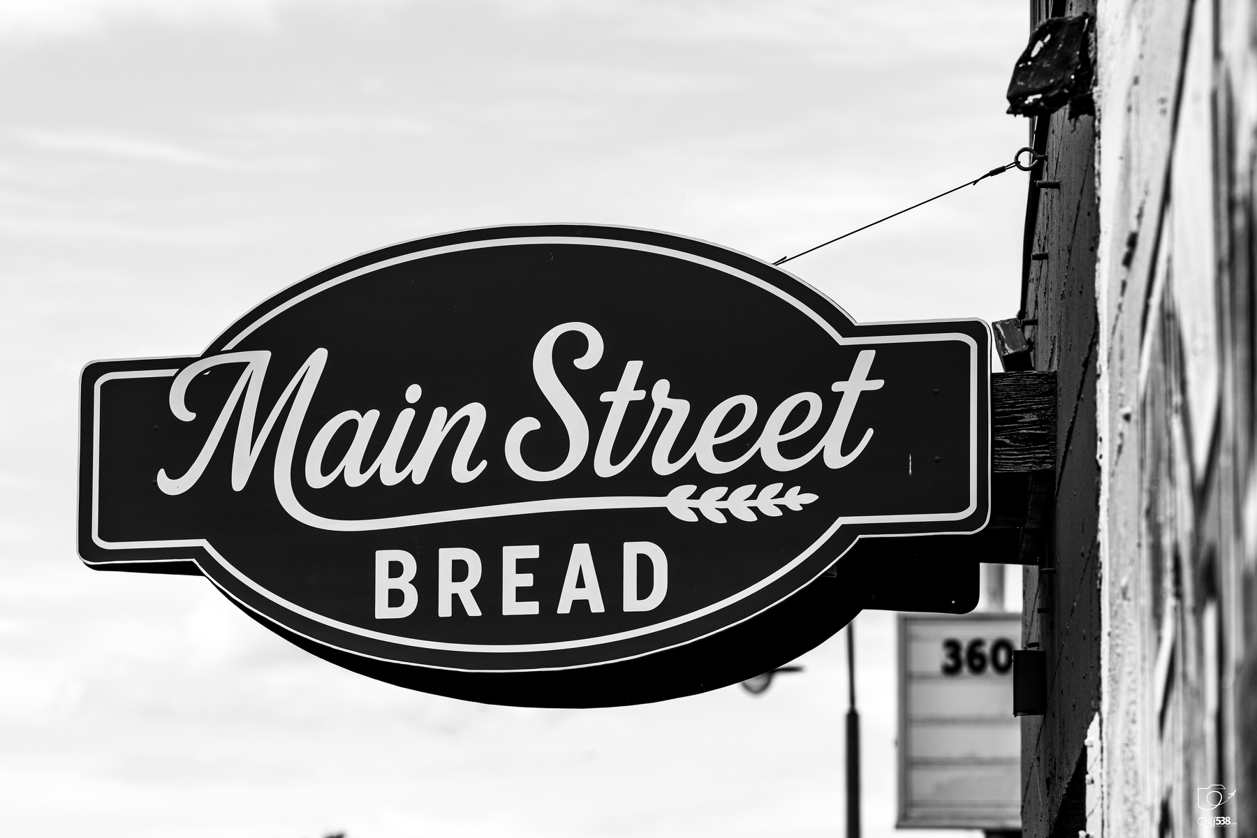 Auto-generated description: A black and white sign for Main Street Bread is mounted on the side of a building.