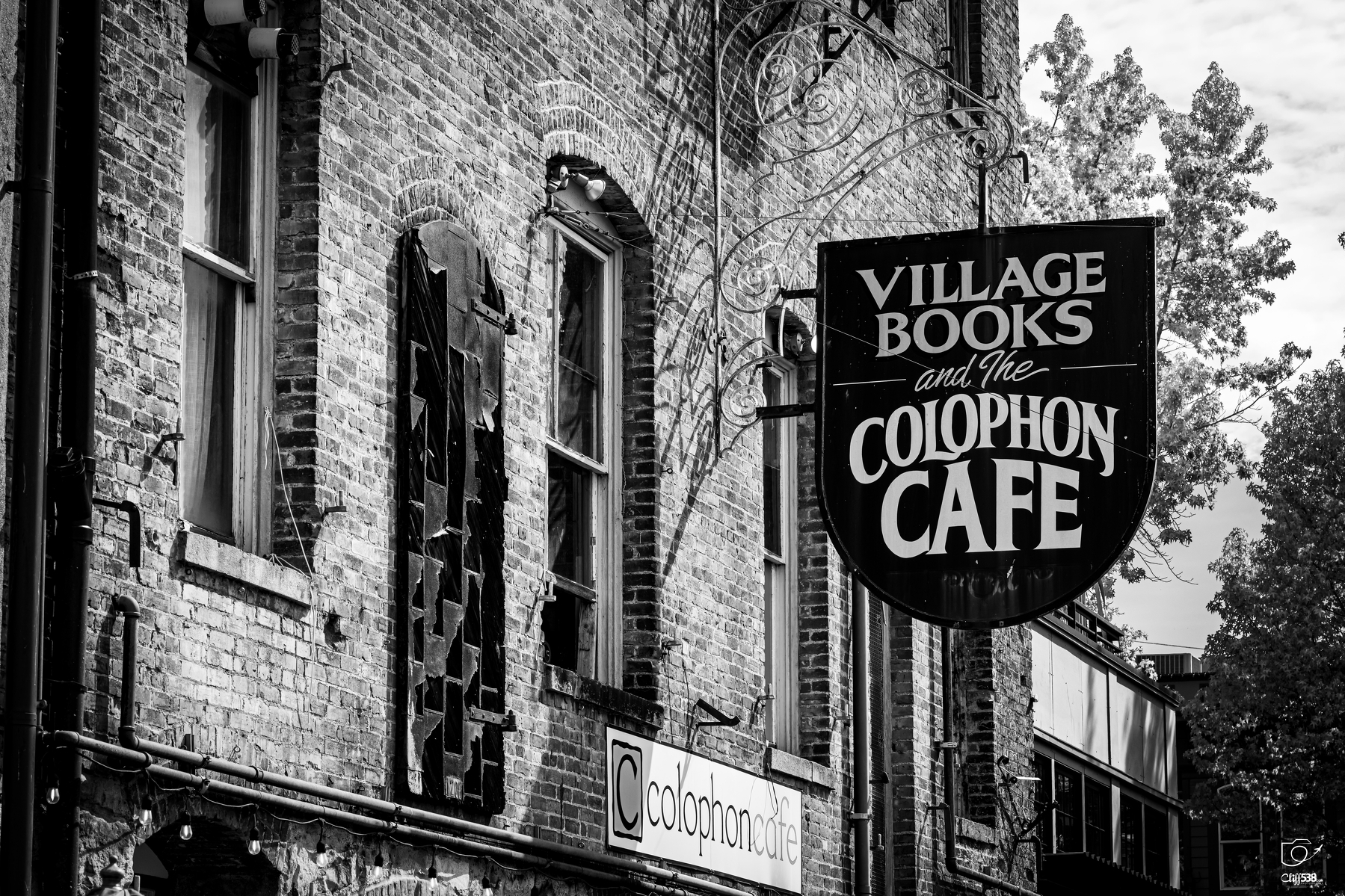 Auto-generated description: A brick building features signs for Village Books and the Colophon Cafe against a backdrop of trees and sky.