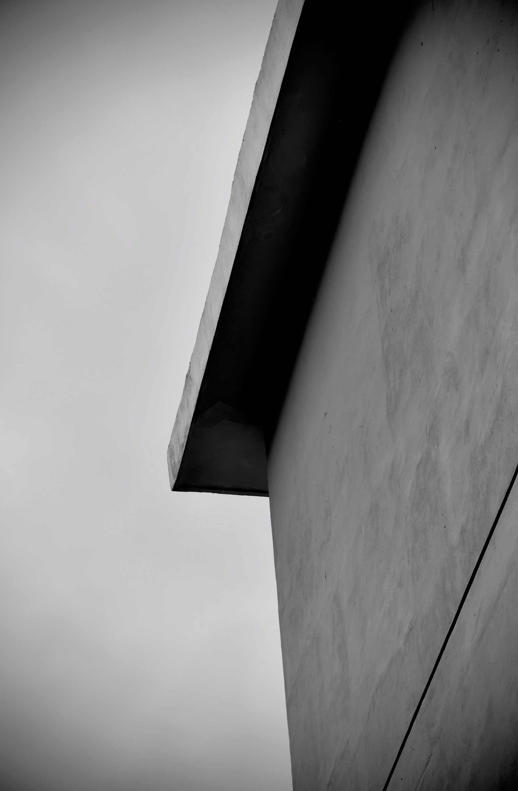 Auto-generated description: A stark, monochrome photograph shows the sharp, angular lines of a modern building against a cloudy sky.