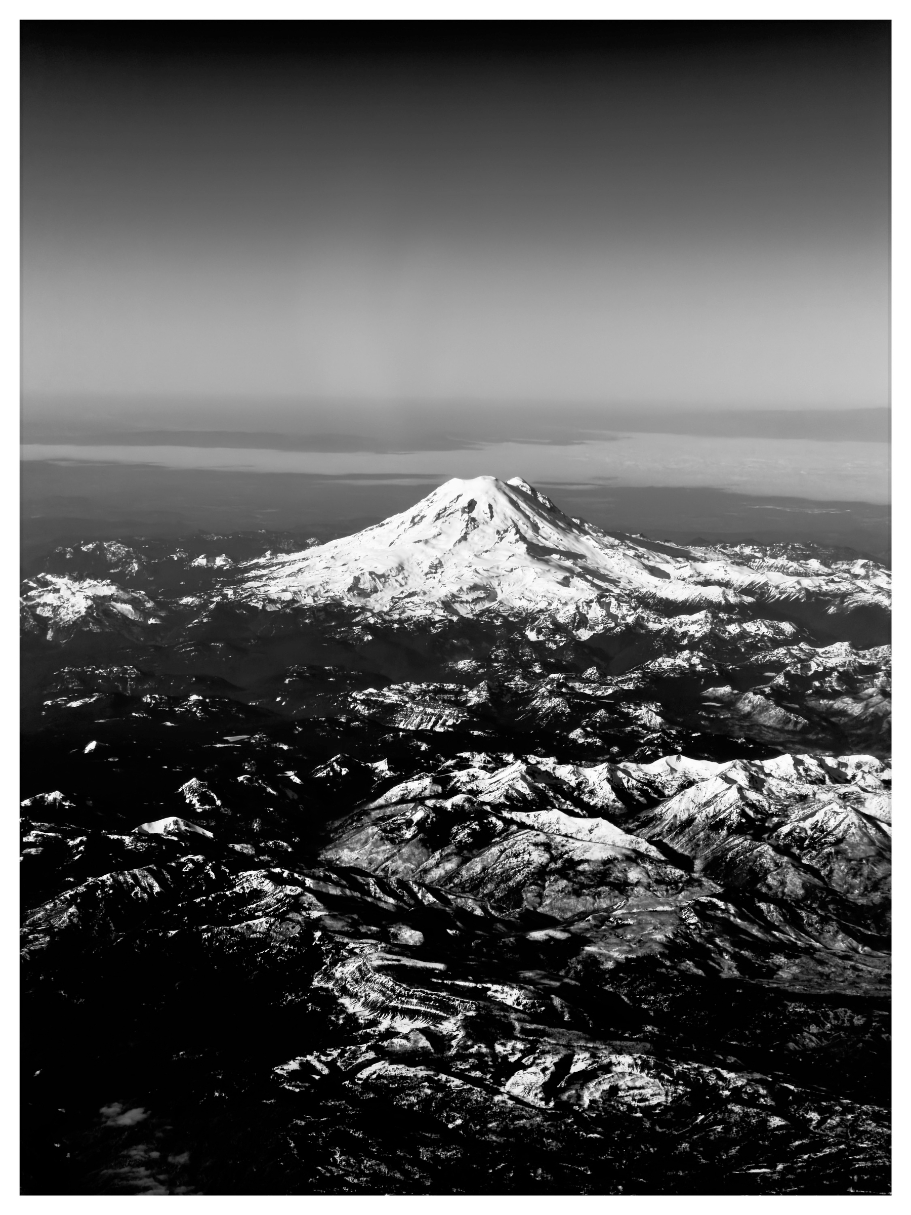 Auto-generated description: A stunning black and white aerial view showcases a snow-capped mountain surrounded by rugged, snowy terrain.