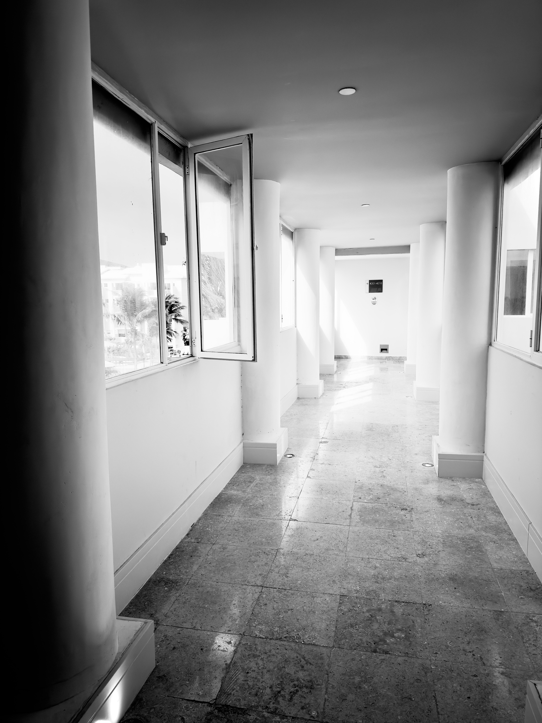 A hallway with large windows and open spaces, showcasing a minimalist design in black and white.